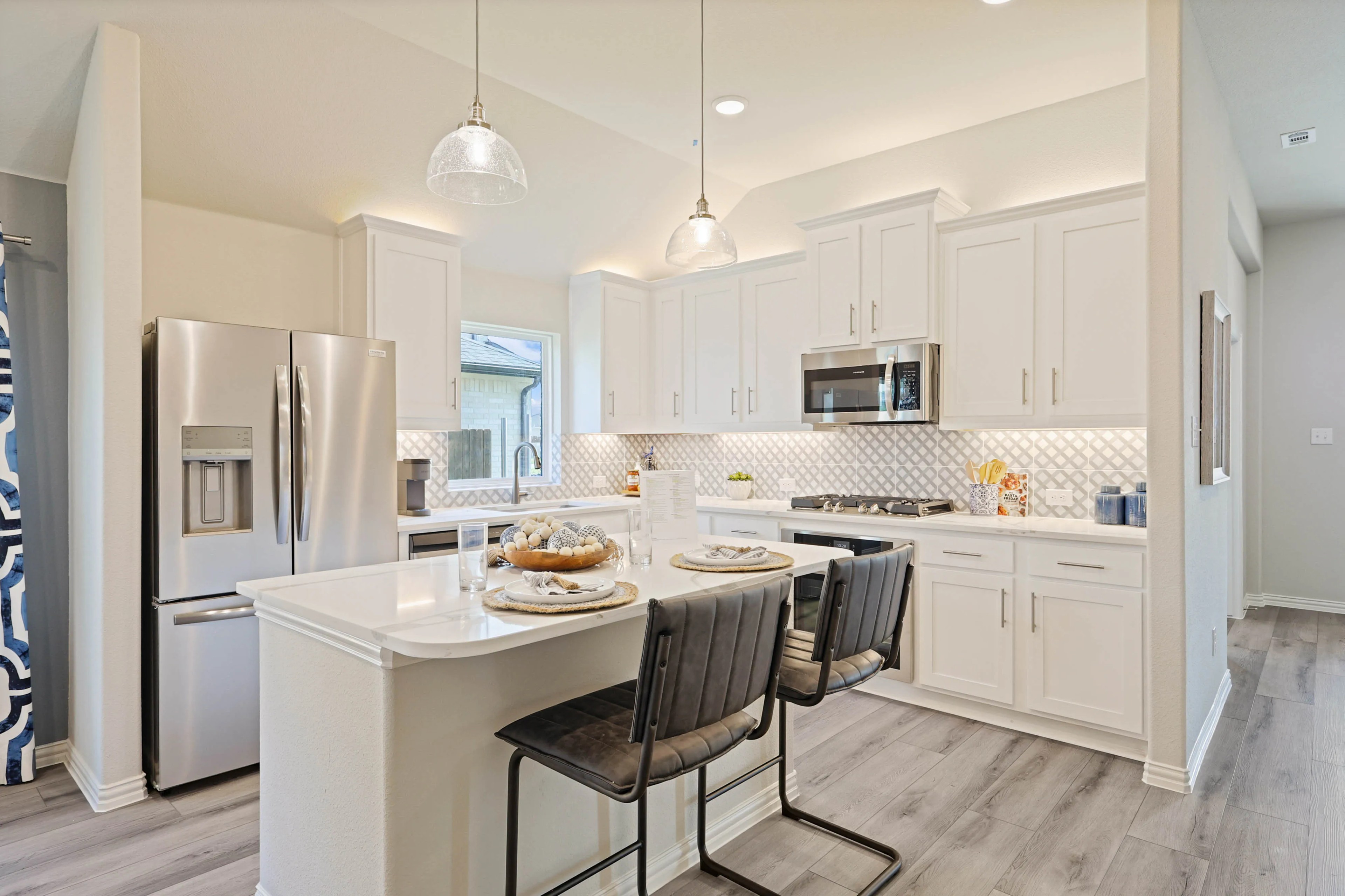 Modern kitchen in Pebblebrook; white cabinets, stainless steel appliances, geometric backsplash, island seating.