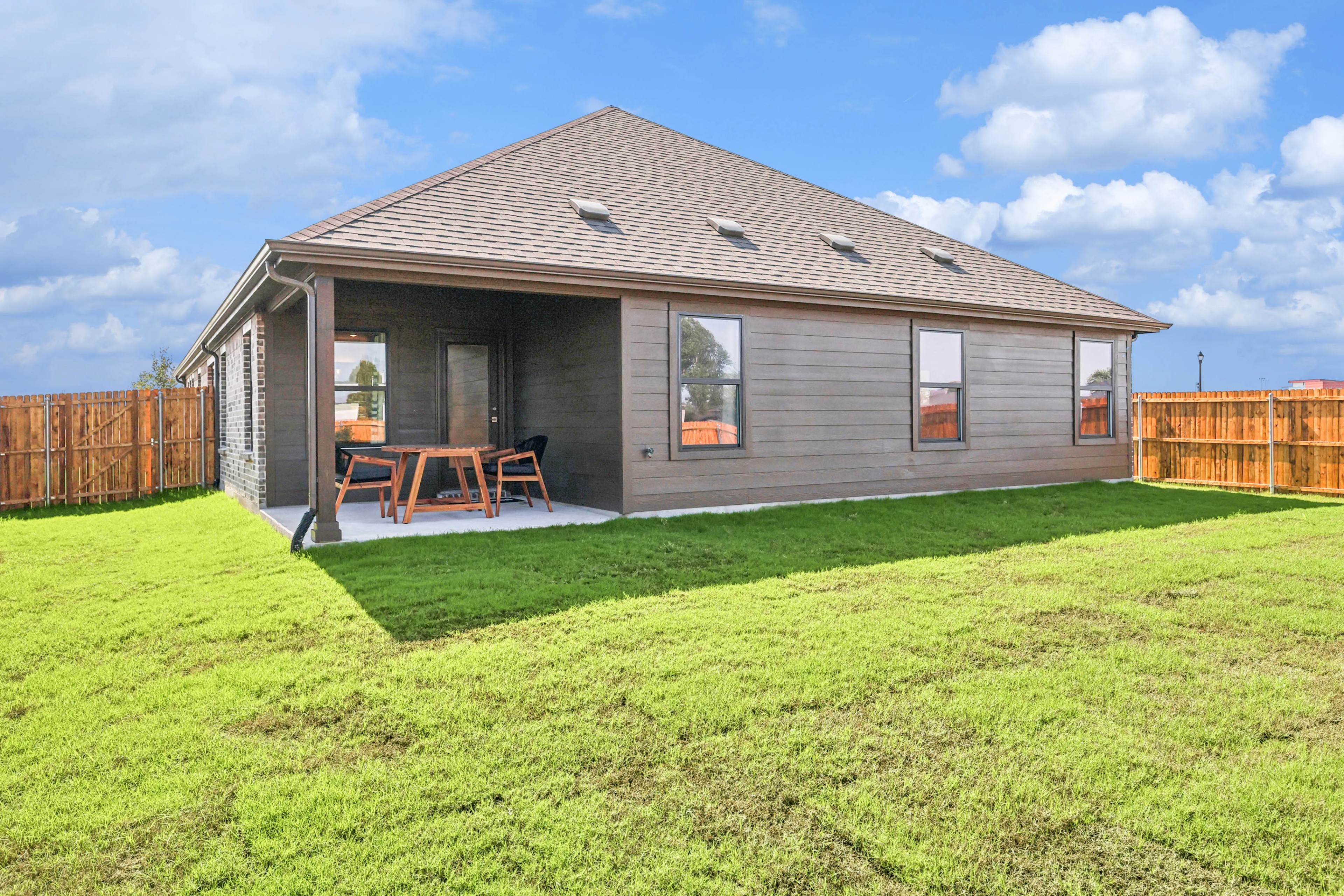 Backyard with covered patio, wood siding, and sloped roof in Pebblebrook community. Fenced yard, open sky.