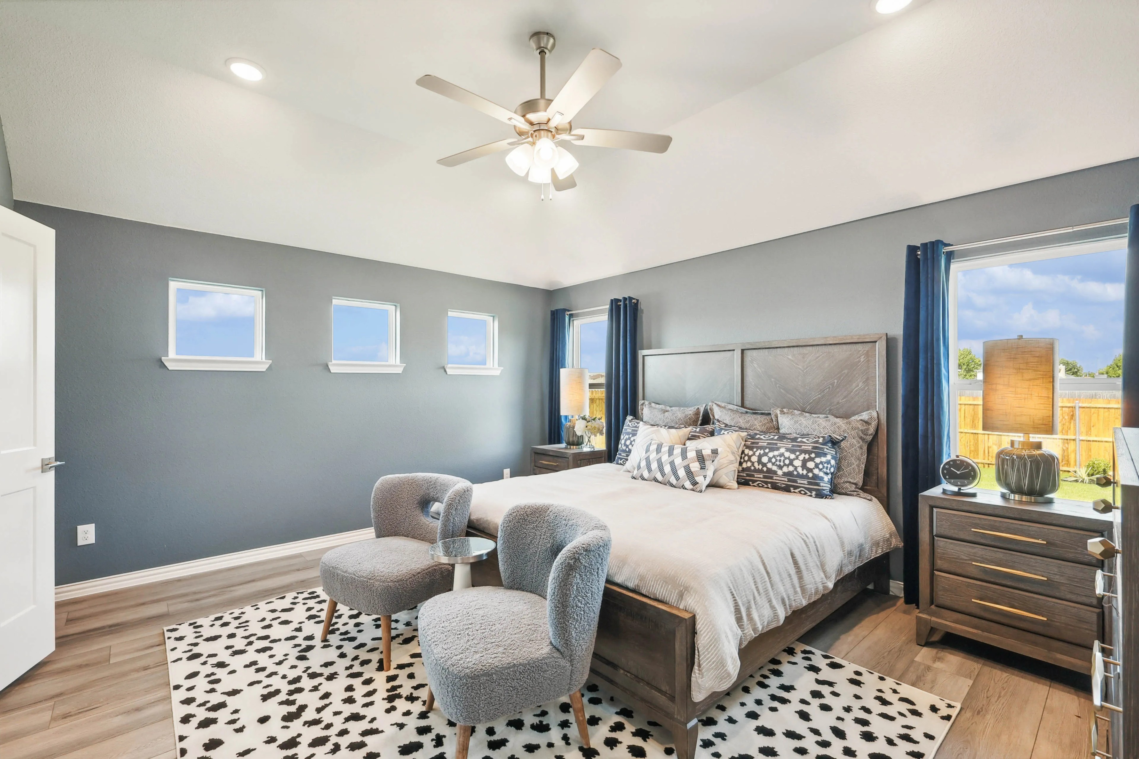Elegant bedroom with gray walls, three small windows, plush bed, and modern decor in Pebblebrook community.
