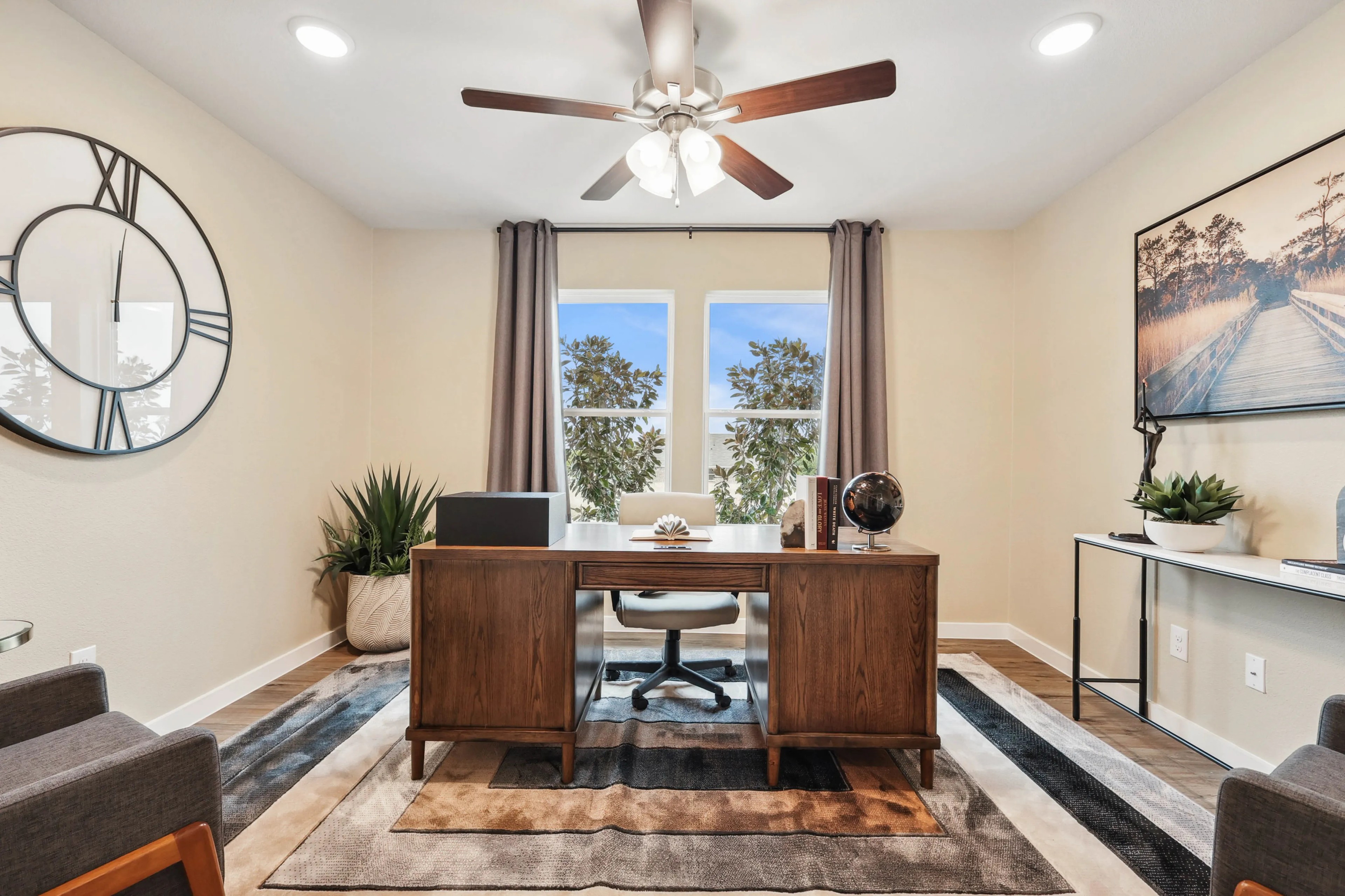 Elegant home office with wood desk, large clock, art, and plants, Simpson Crossing community.