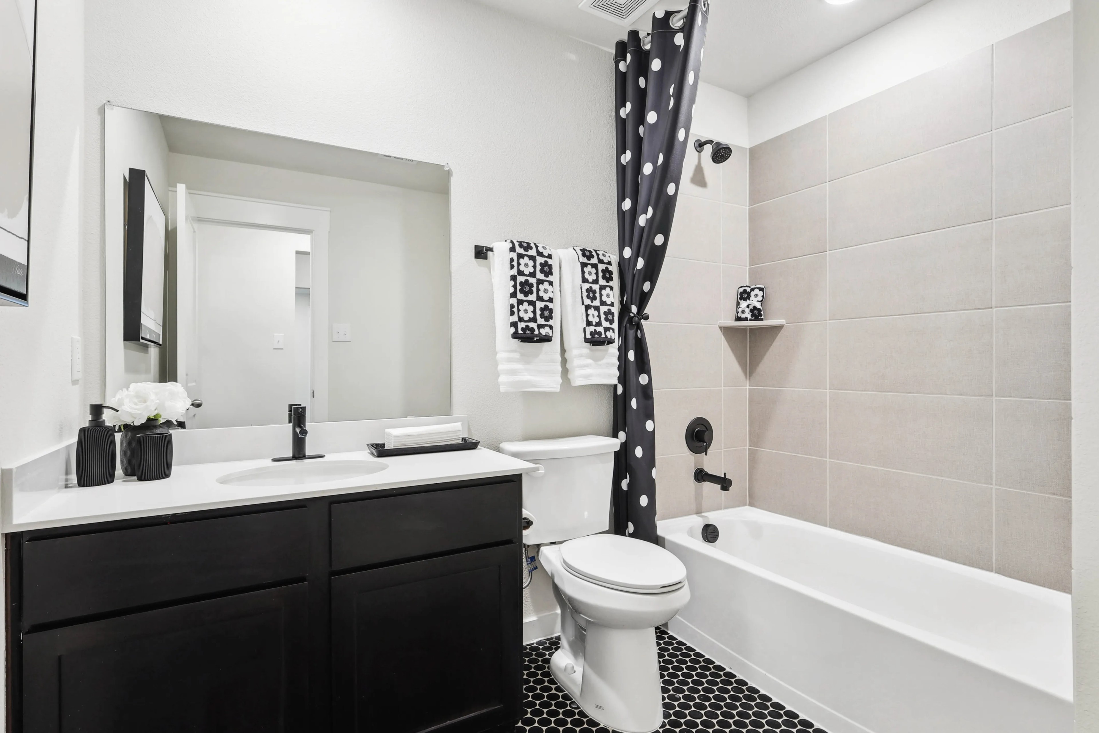 Modern bathroom with black vanity, polka dot curtain, hex tile floor, in Simpson Crossing. Neutral palette with sleek fixtures.
