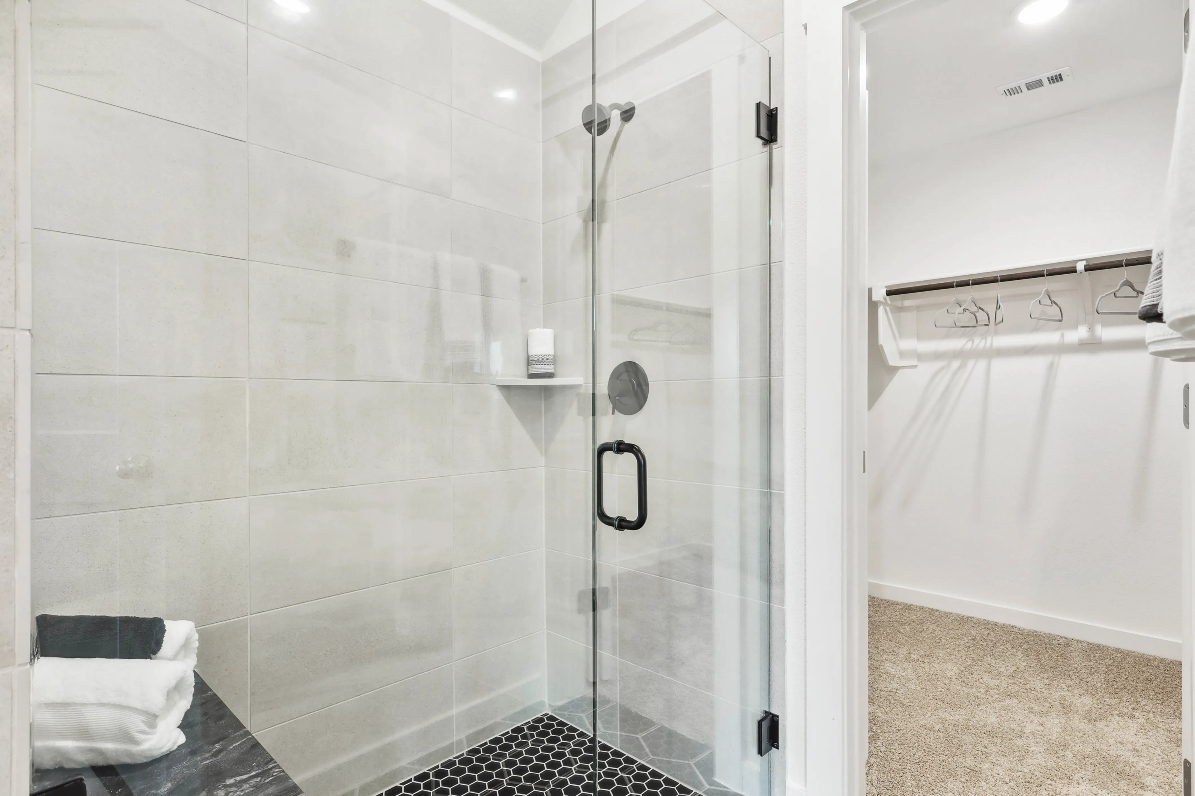 Glass shower with black fixtures and hex tile flooring beside walk-in closet, Simpson Crossing.