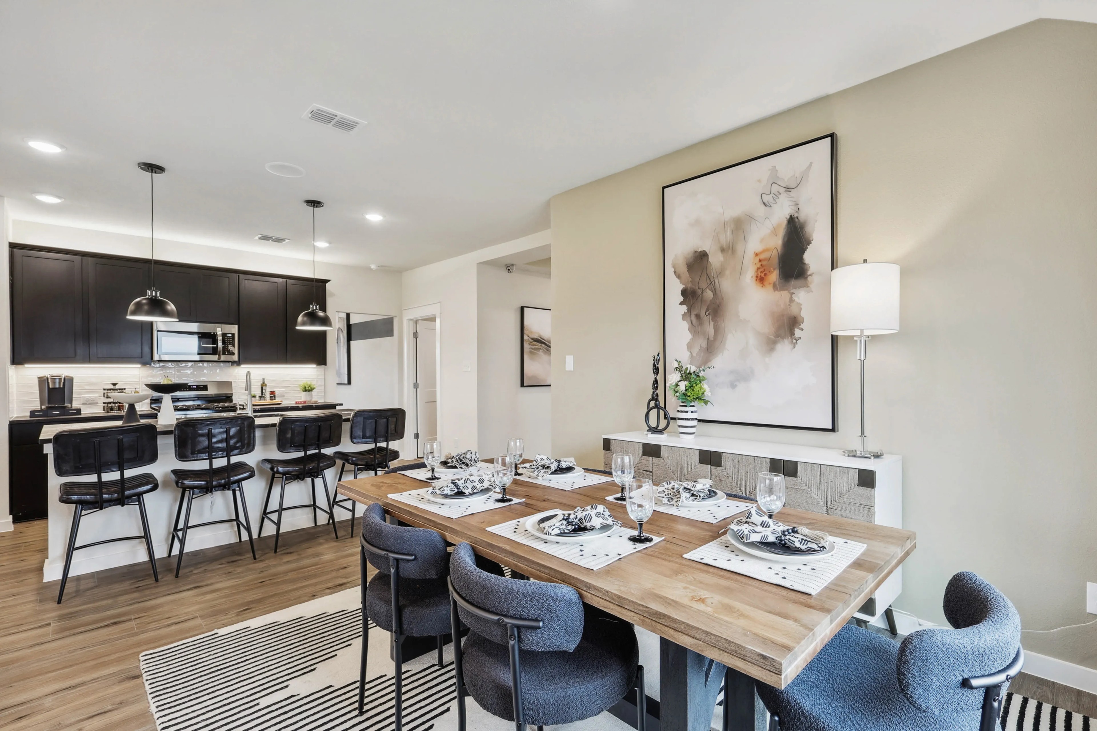 Open-plan dining room with wood table, plush chairs, abstract art, and modern kitchen in Simpson Crossing home.