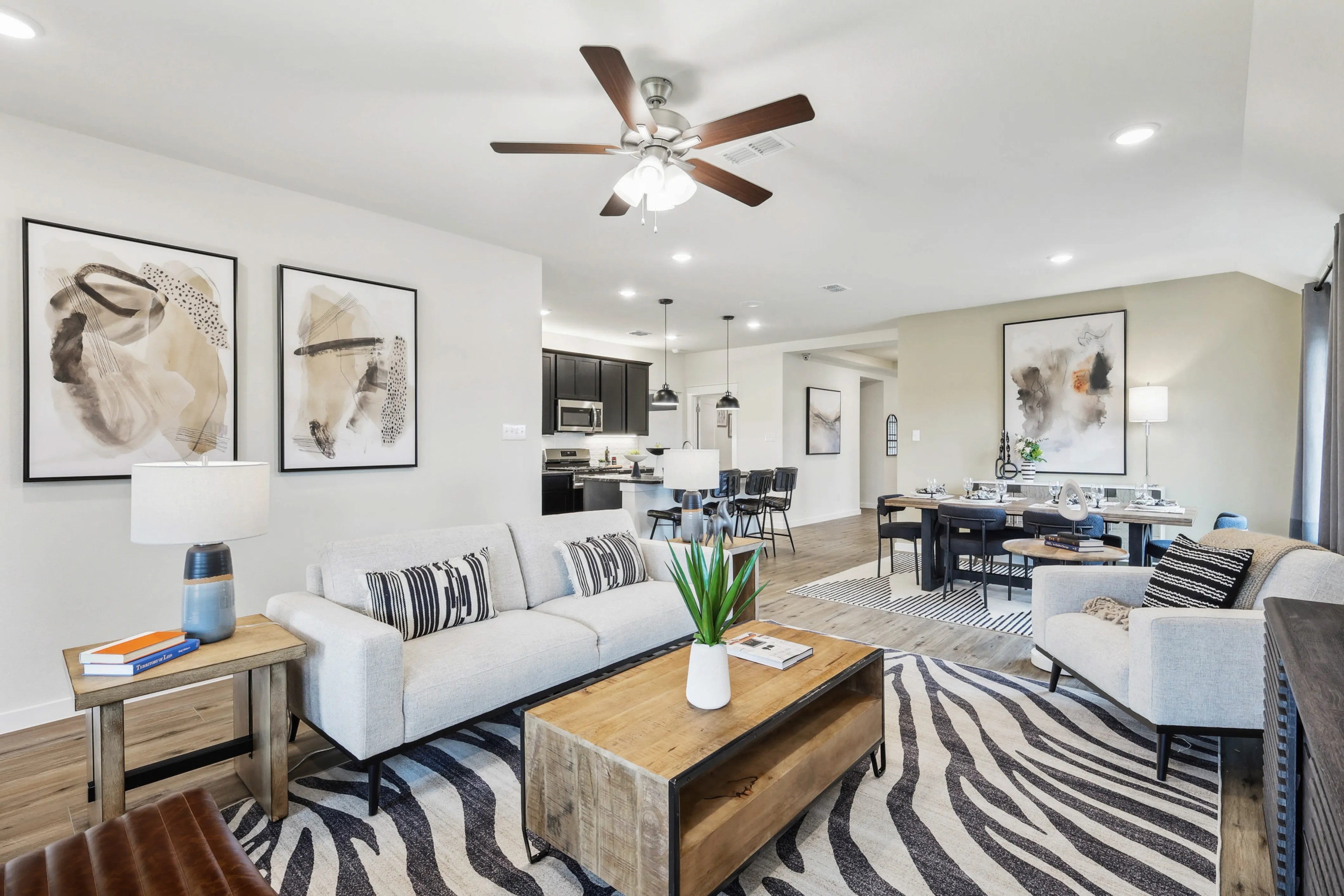 Modern open-concept living room with elegant decor, Simpson Crossing. Features abstract art, wood floors, ceiling fan.