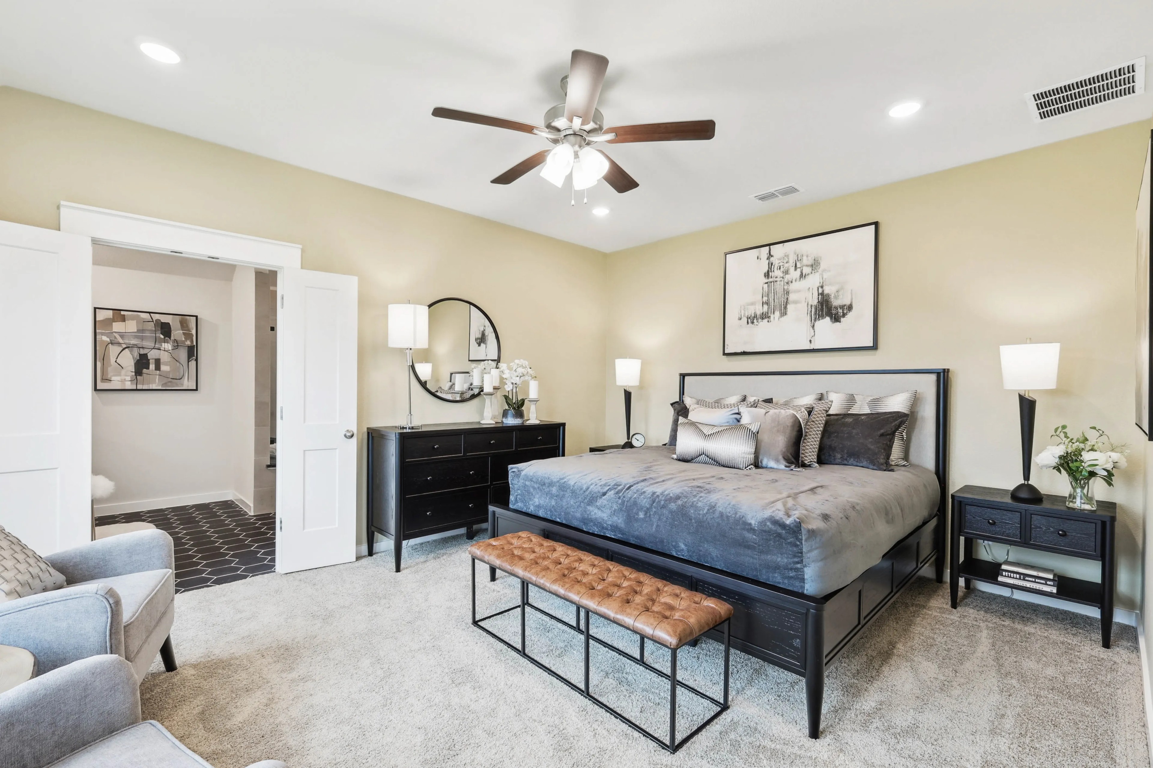 Luxury bedroom with beige walls, dark furniture, and plush bedding in Simpson Crossing. Wall art and ceiling fan present.