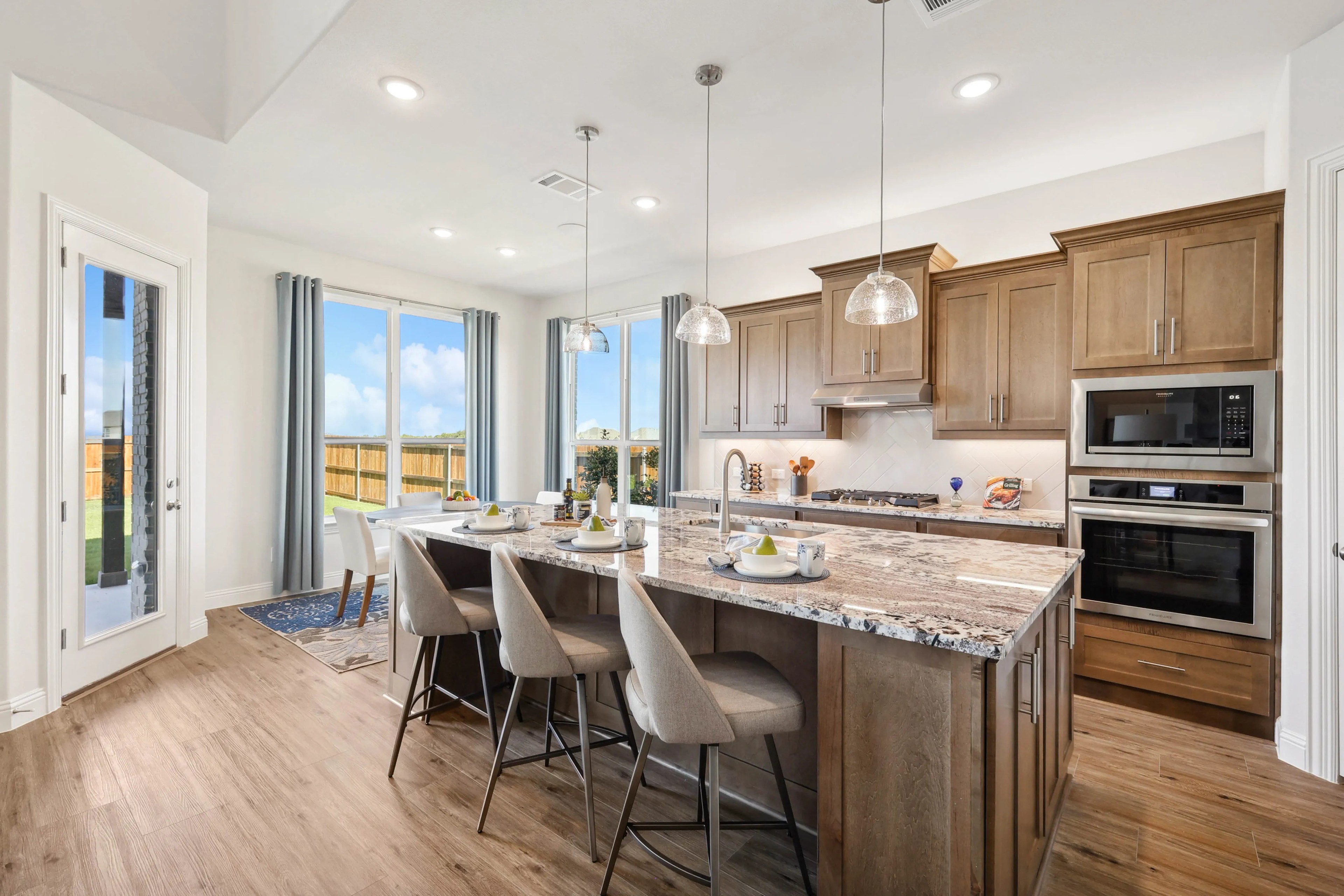 Modern Ridge Crossing kitchen with granite island, wood cabinets, pendant lights, and large windows. Open airy design.