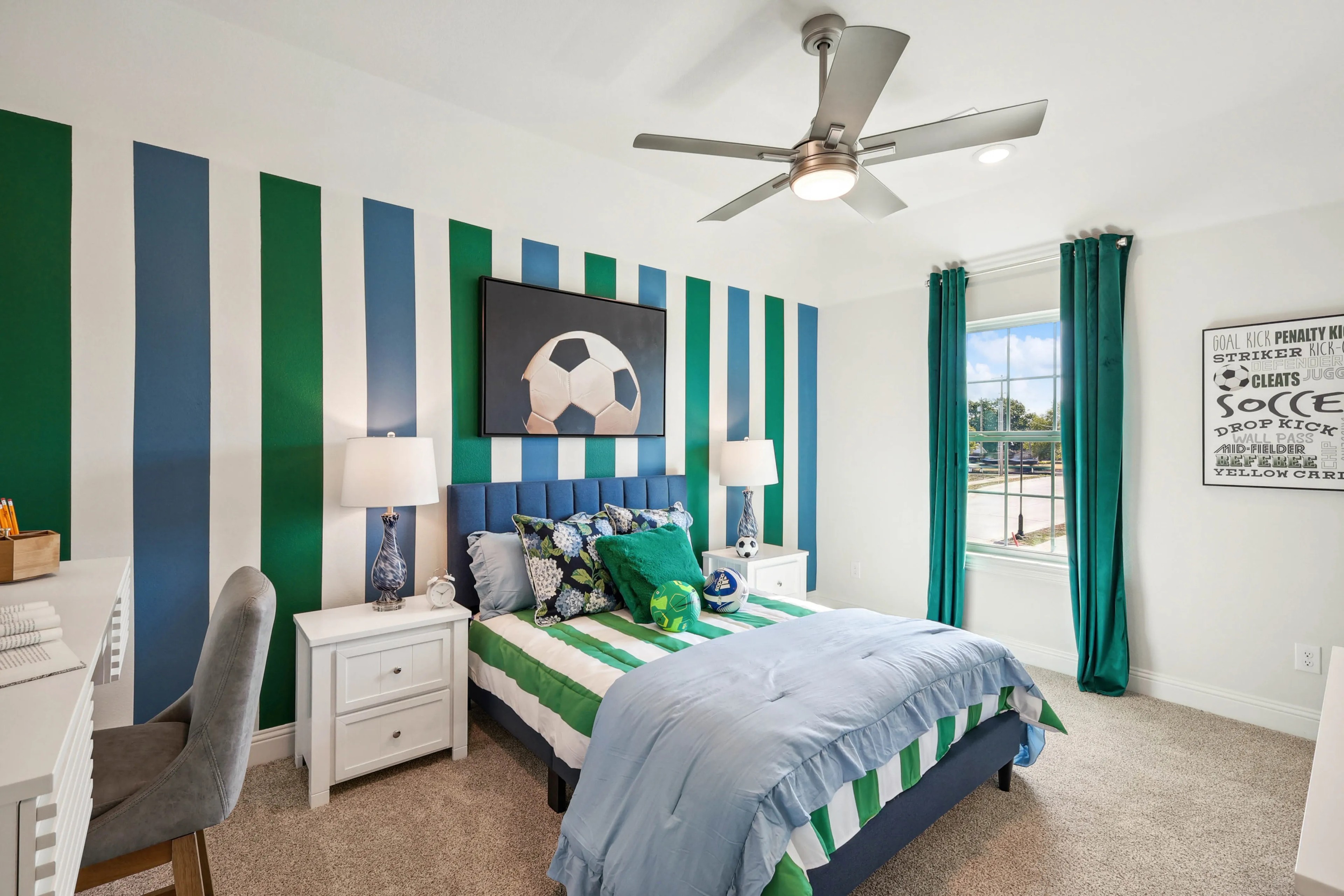 Modern bedroom with striped blue, green walls, soccer theme, at Ridge Crossing community. Large window, ceiling fan.