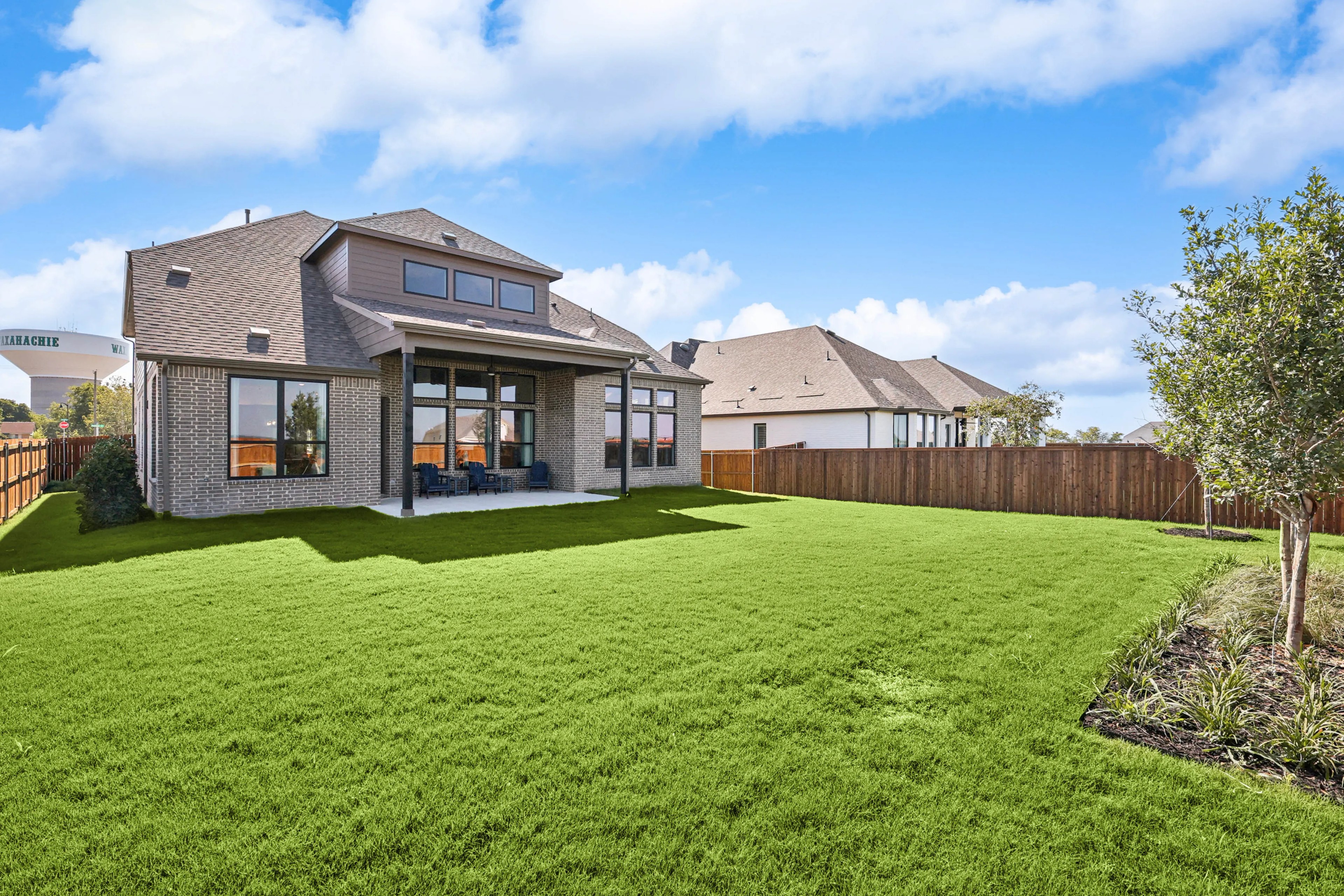 Spacious brick home with large windows, gabled roof, and lush lawn in Waxahachie. Ridge Crossing community.