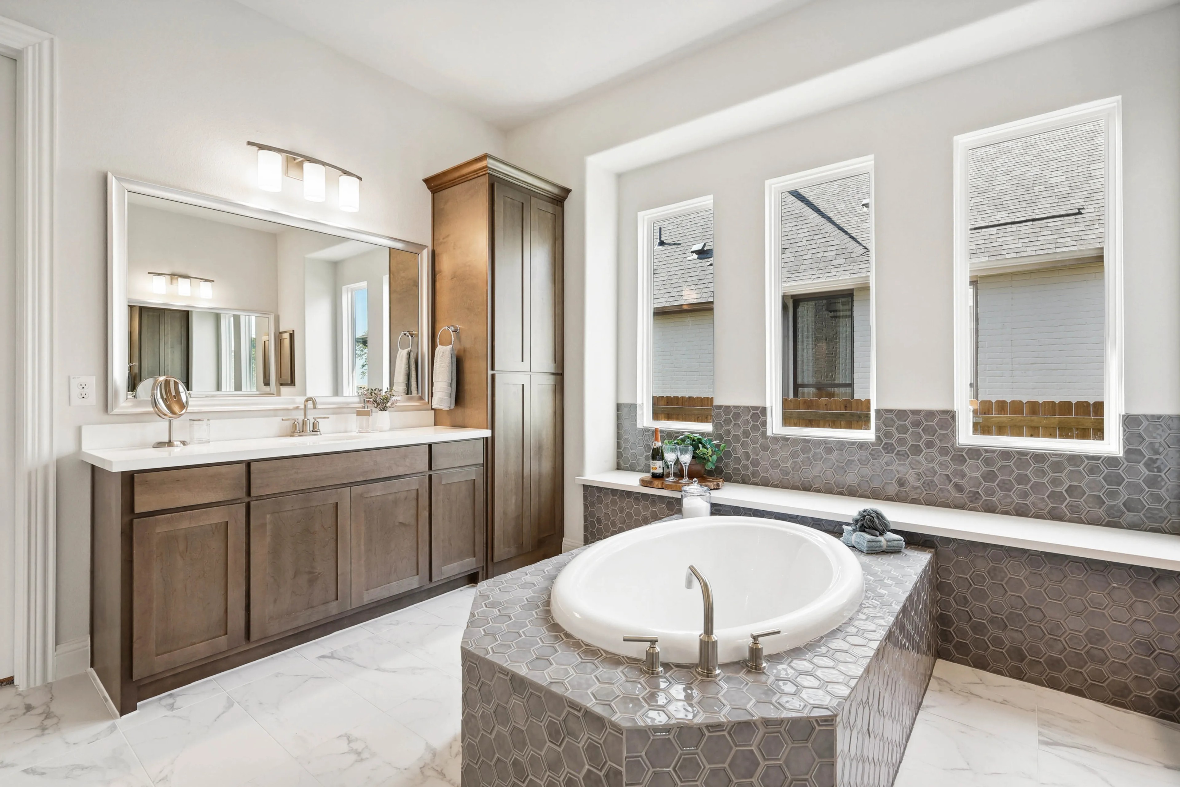 Luxurious bathroom with oval tub, hex tile, large mirrors, wooden cabinets in Ridge Crossing.
