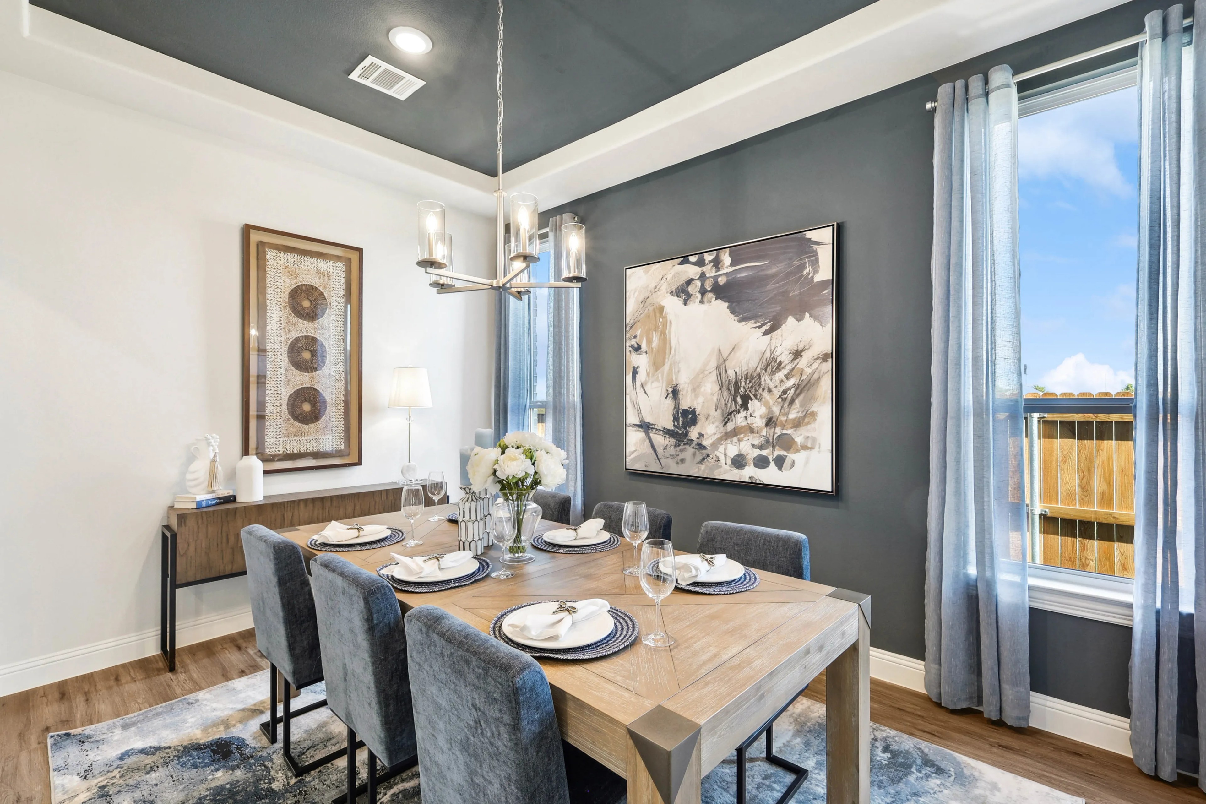 Elegant dining room with abstract art, wooden table, velvet chairs, chandelier, located in Ridge Crossing community.