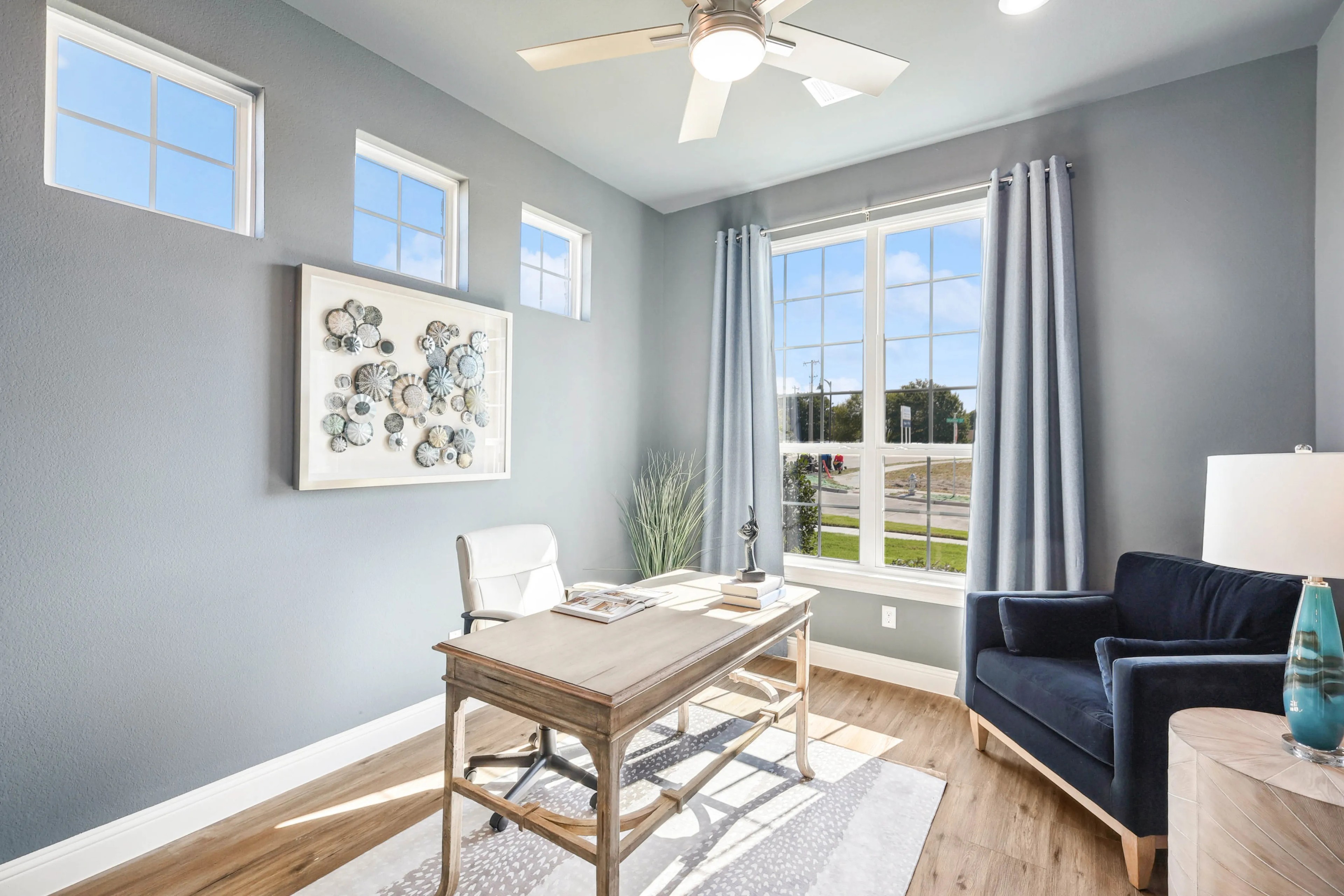 Elegant home office with large windows, modern ceiling fan, and stylish decor in Ridge Crossing community.