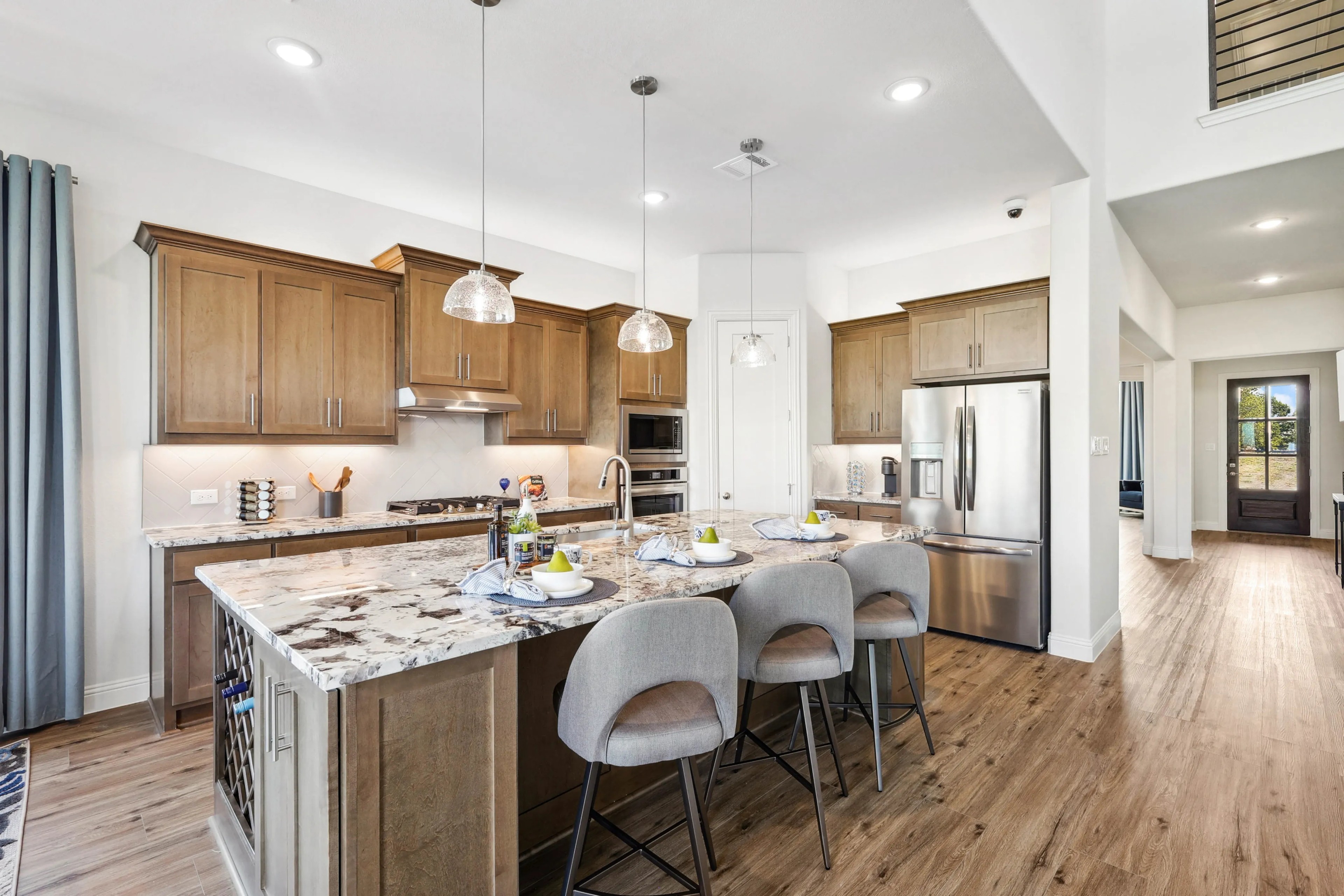 Modern kitchen in Ridge Crossing with wooden cabinets, marble island, stainless steel appliances, pendant lights.