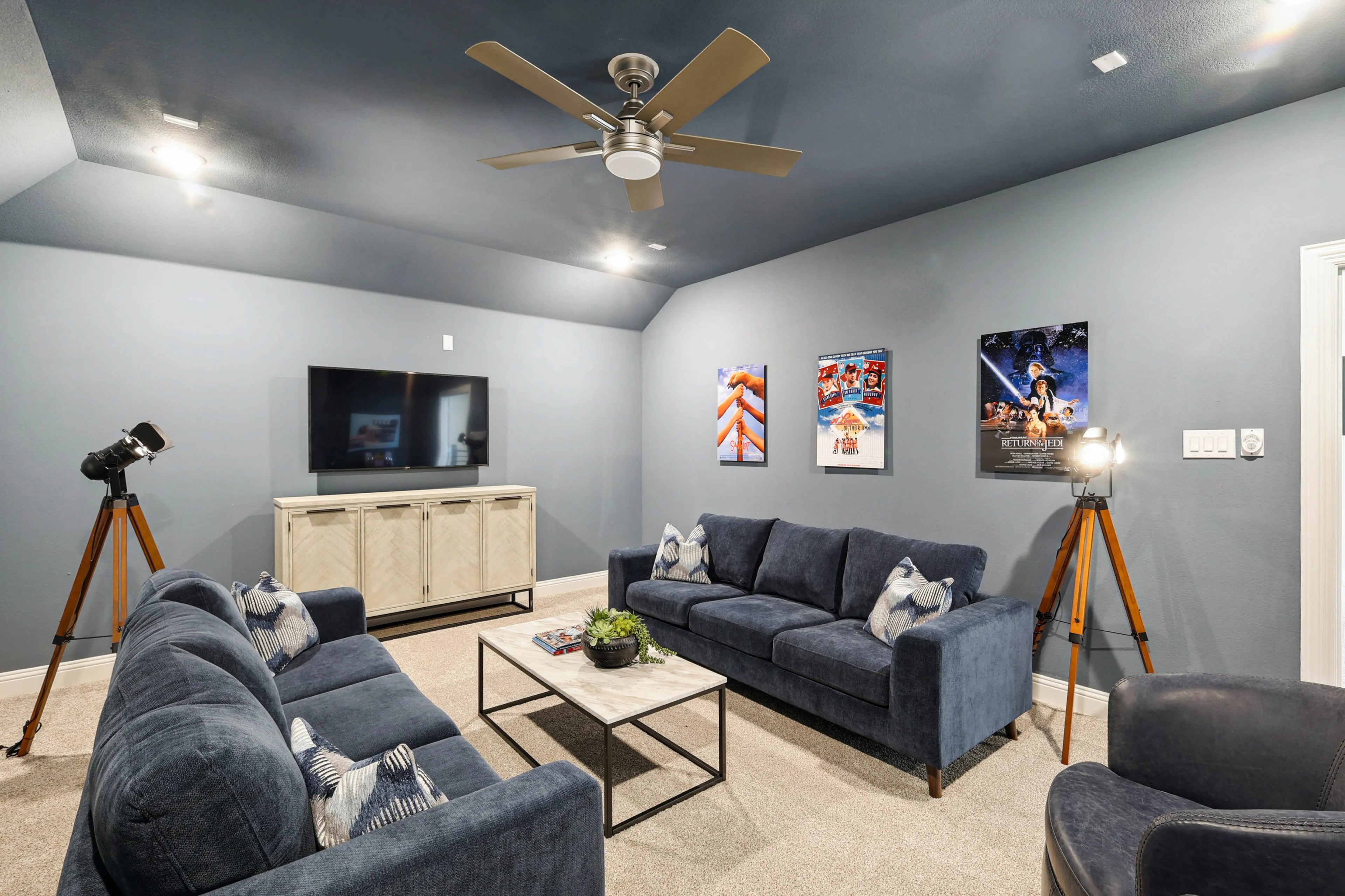 Luxurious media room with plush navy sofas, modern lighting, and movie posters in Ridge Crossing community.