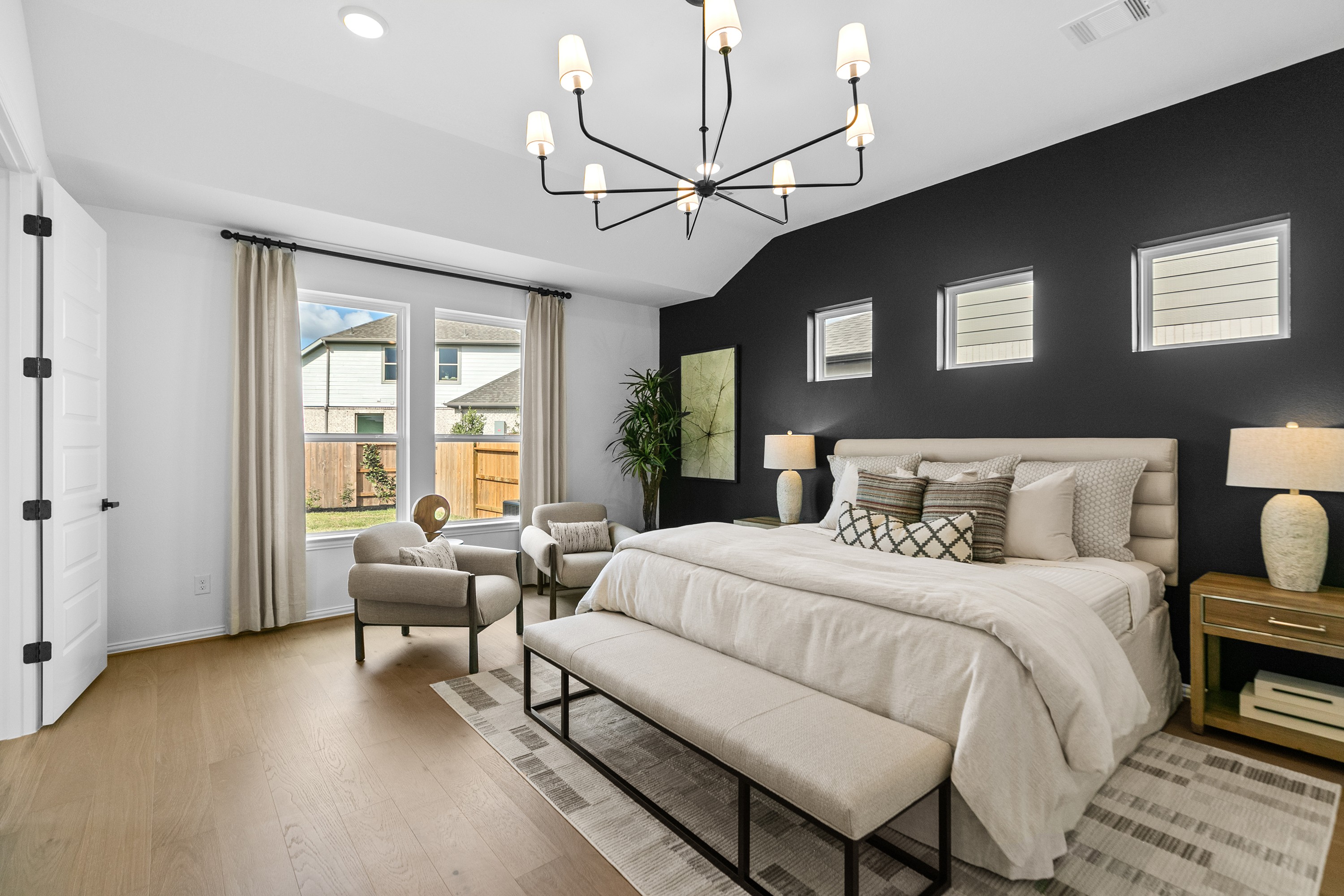Elegant bedroom with black accent wall, chandelier, large windows. Luxurious design in River Ranch community.