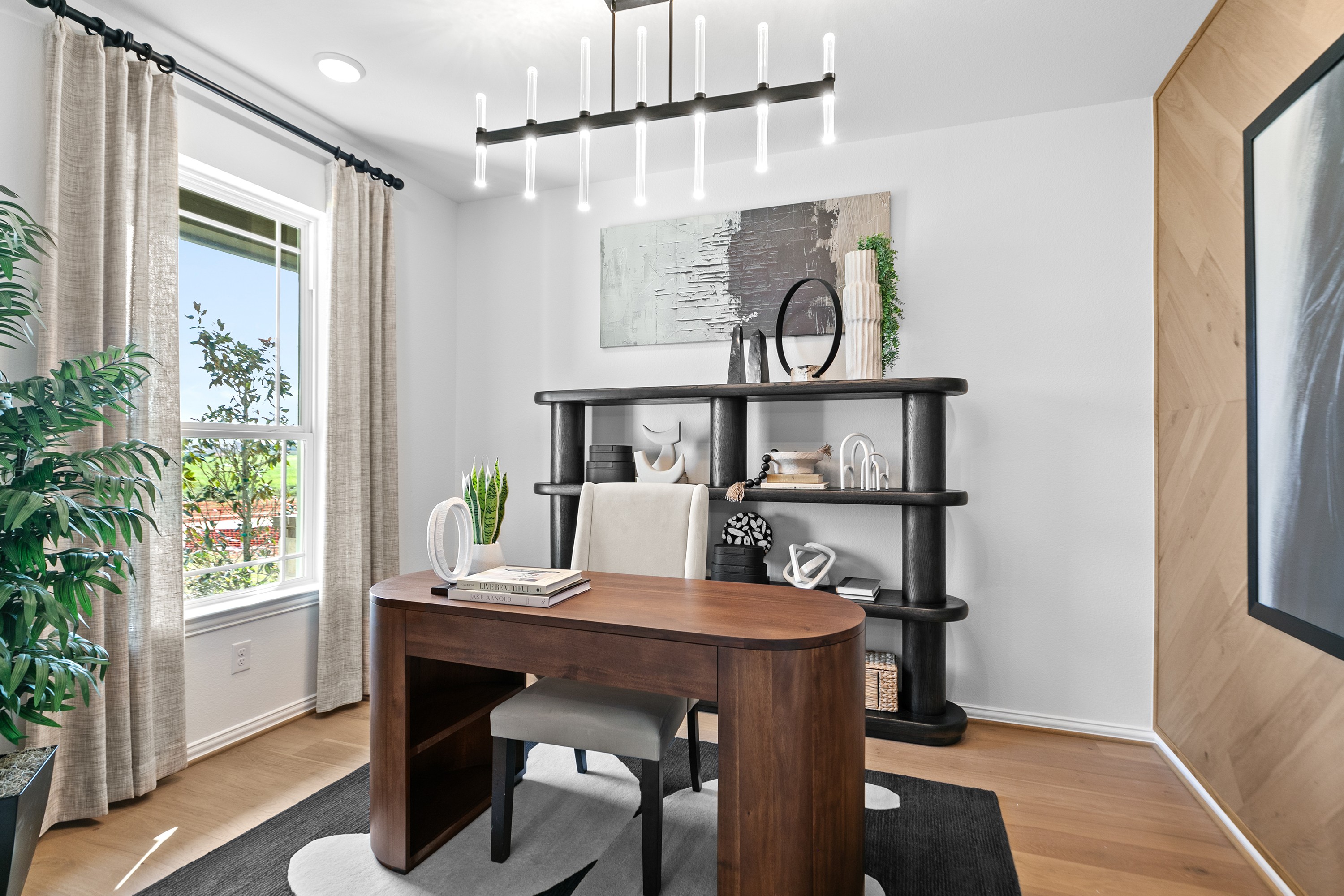 Modern home office with wood desk, unique chandelier, and open shelving in River Ranch community. Large window with curtains.