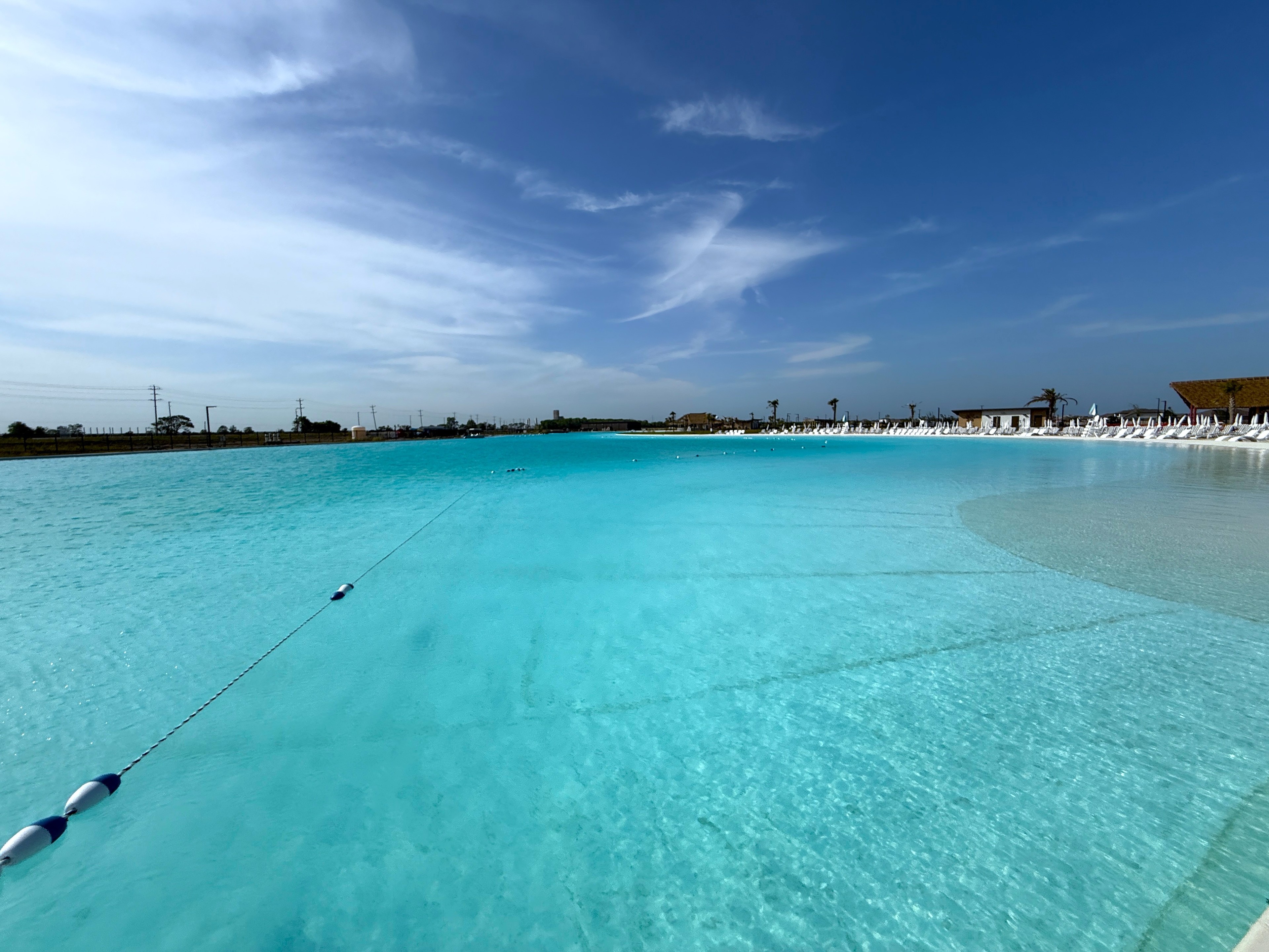 Crystal-clear lagoon with sandy shore, lounge chairs, and palm trees, River Ranch community, under a clear blue sky.