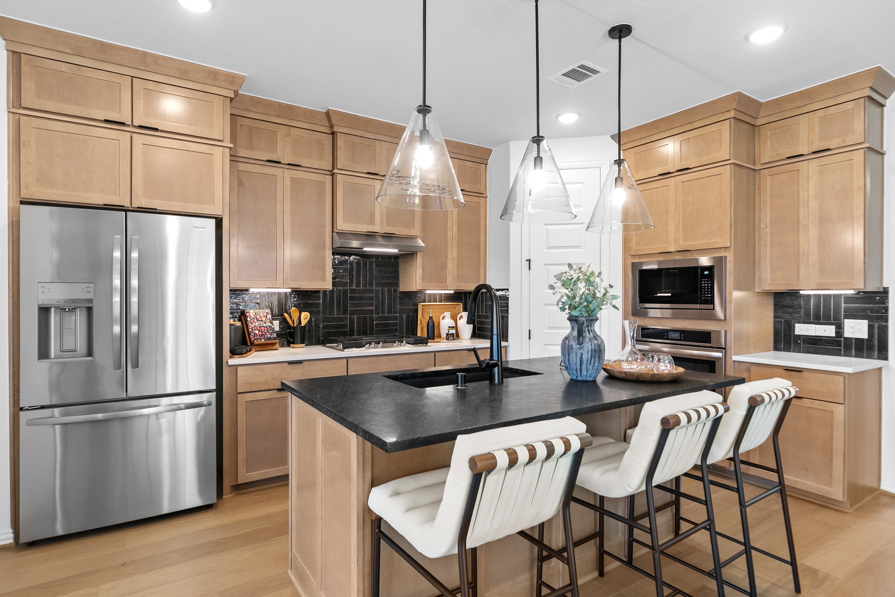 Modern kitchen with wooden cabinets, black island, and pendant lights in River Ranch community.