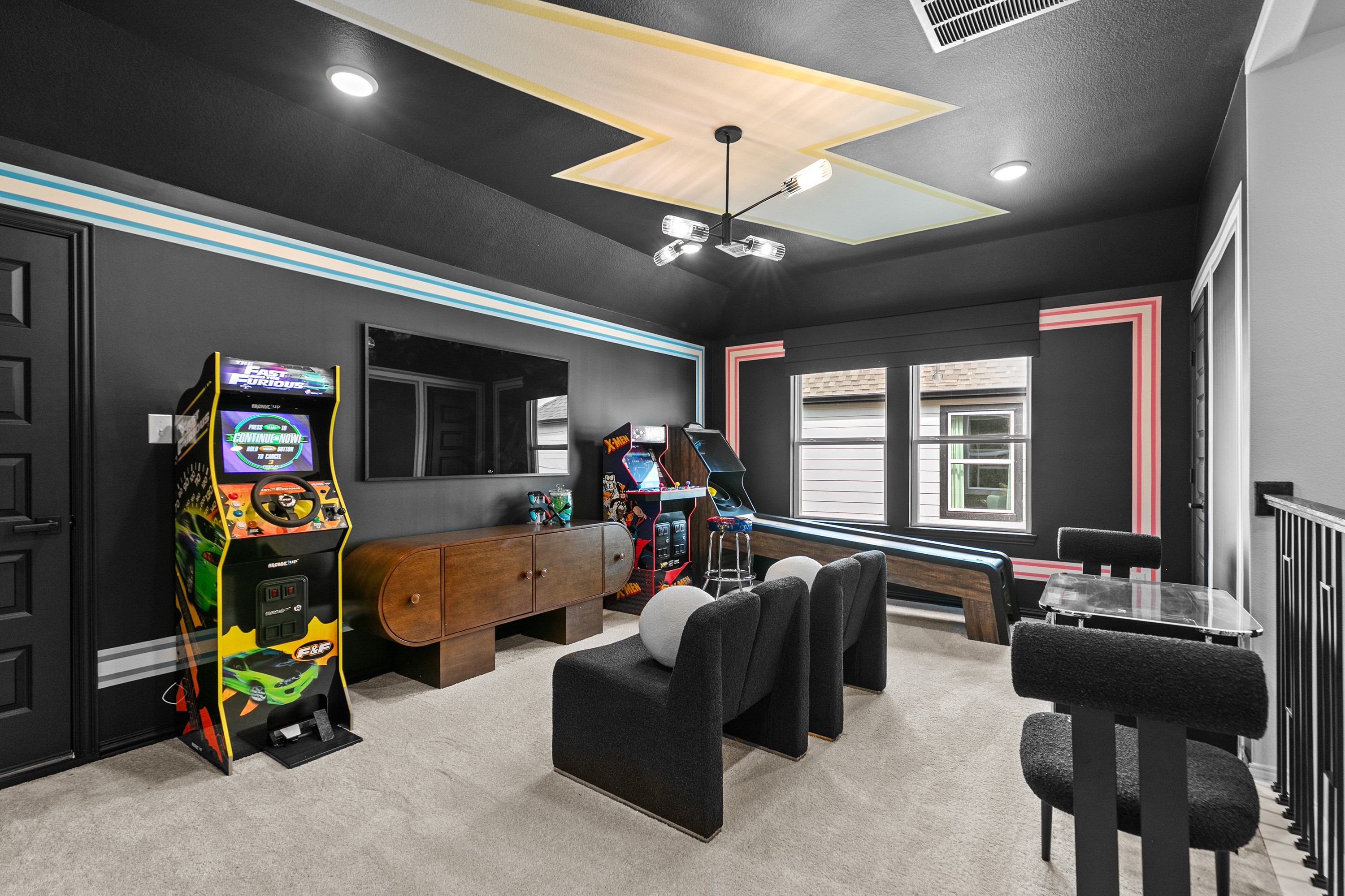 Game room in River Ranch with arcade machines, plush seating, modern decor, and geometric ceiling design.