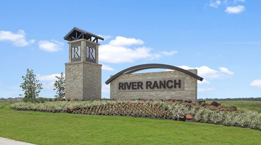 Stone monument with "River Ranch" sign, arched metal feature, landscaped garden, Texas community.