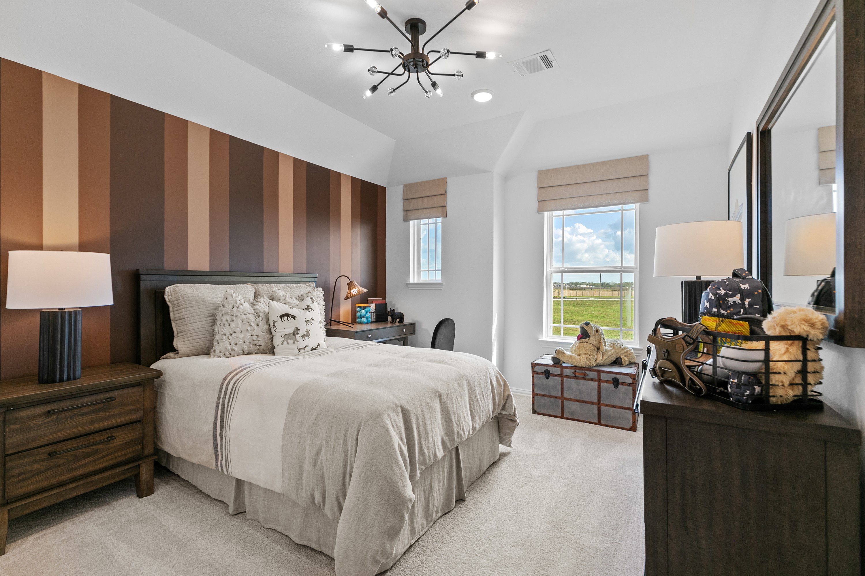 Bedroom with modern chandelier, striped wall, and large windows in River Ranch community.