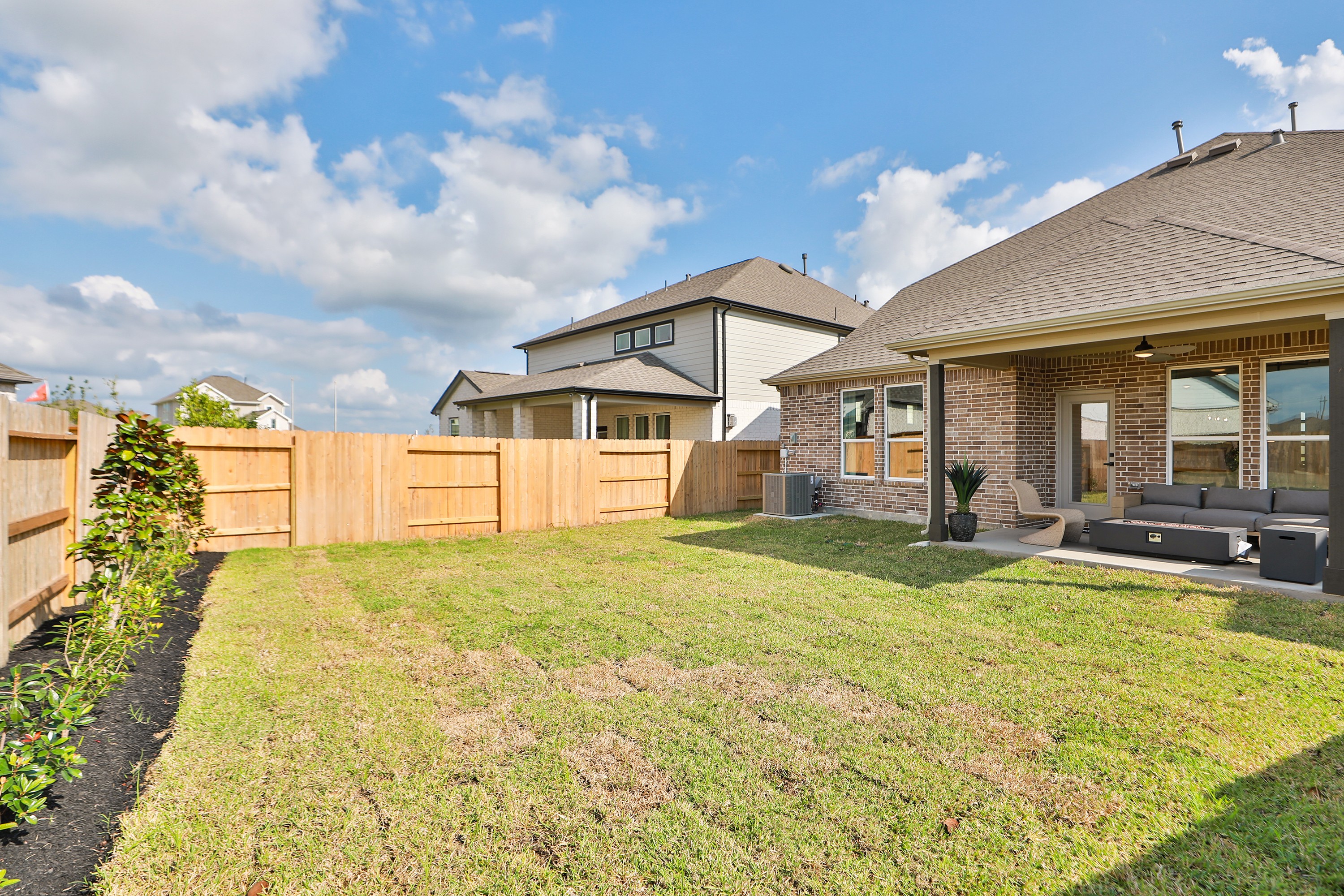 Backyard with brick patio, wooden fence, and seating area in River Ranch community, featuring blue sky.
