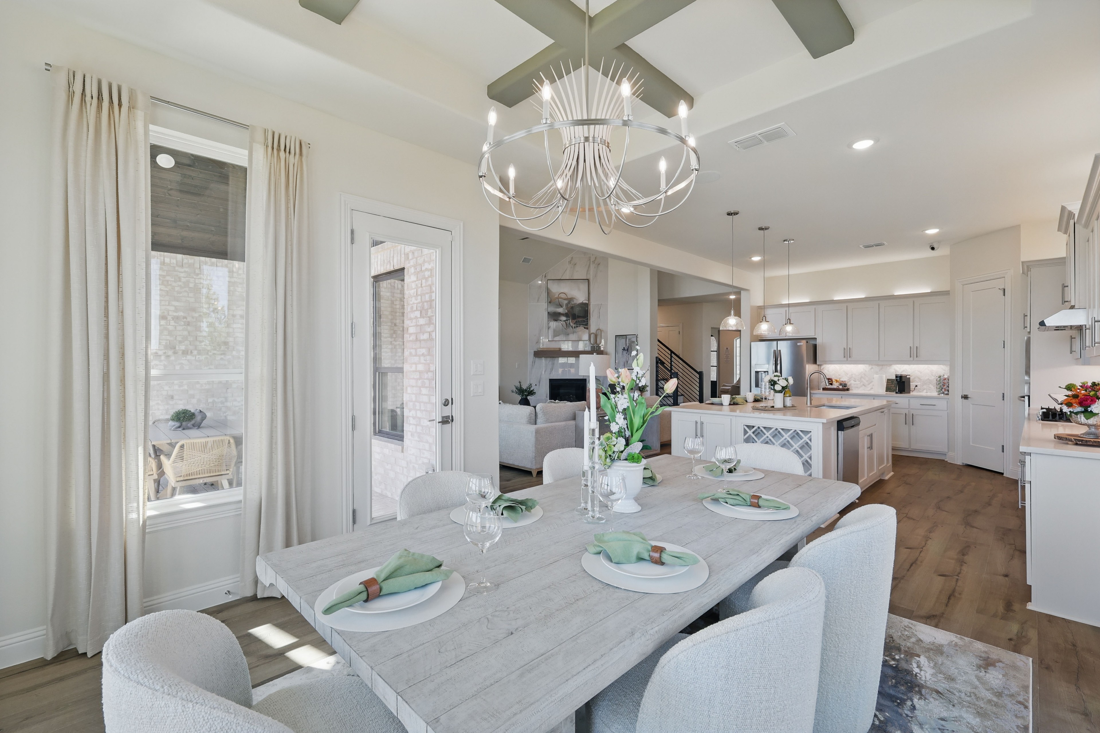 Modern dining room with light wood table, elegant chandelier, and open kitchen at Kelly Ranch, Rio Vista community.