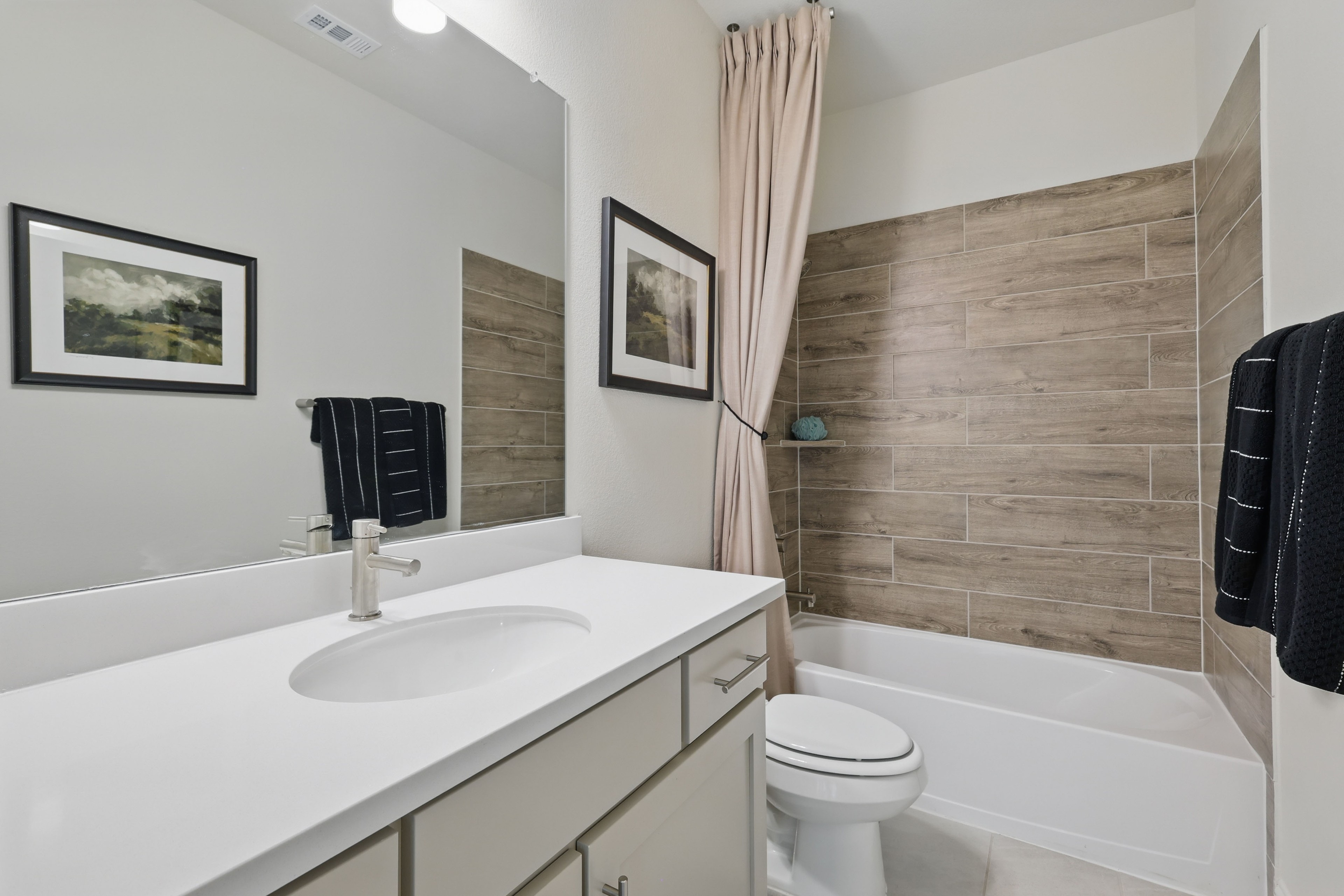 Modern bathroom with wood-patterned tiles, white vanity, and mounted artwork at Rio Vista, Kelly Ranch.