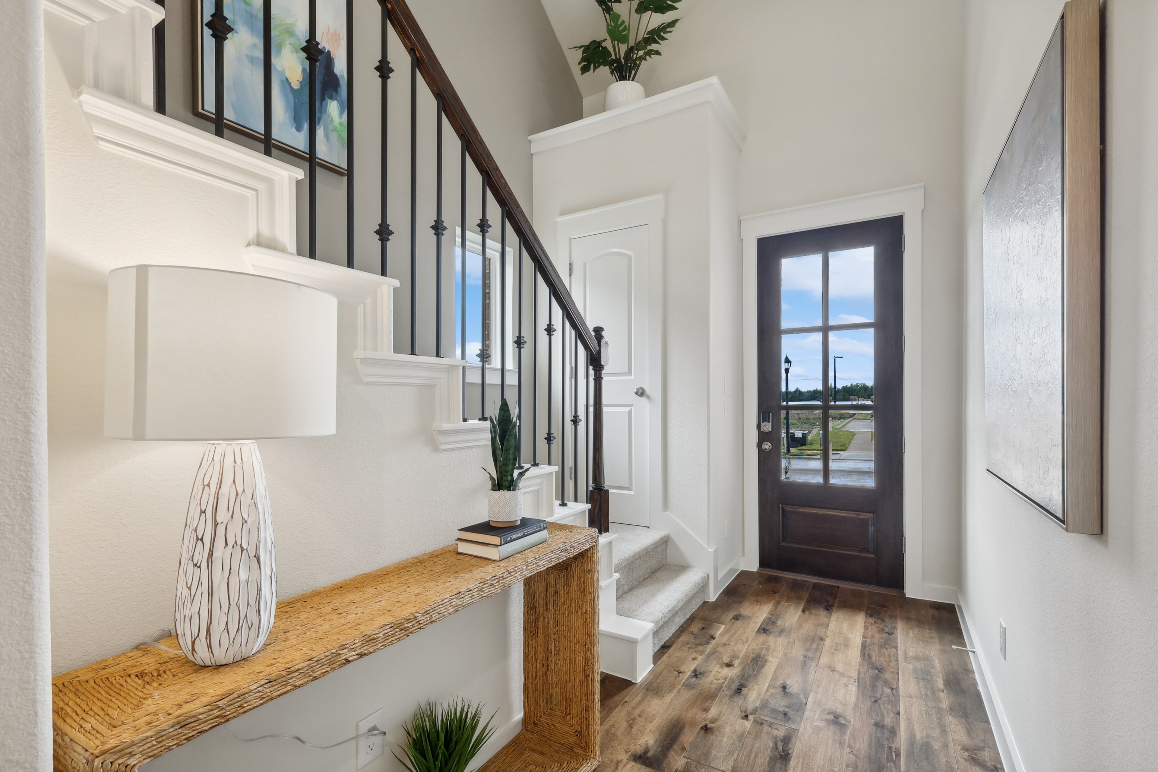 Elegant foyer in Churchill features wood flooring, white stairway with iron balustrade, modern decor, natural light.