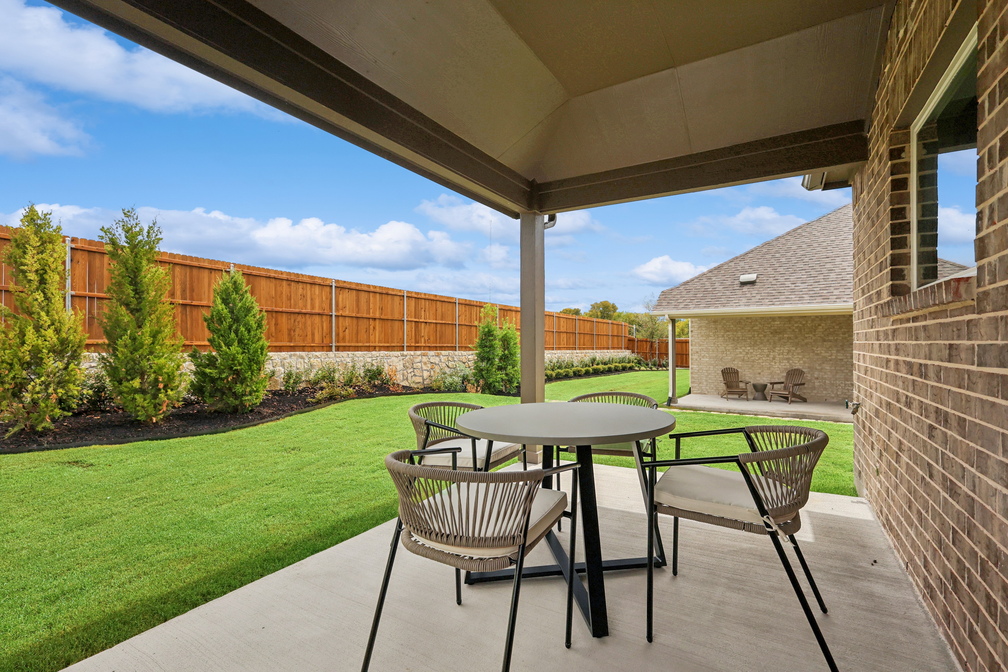 Backyard patio with modern furniture, brick wall, lush lawn, and cedar fence in Churchill community.
