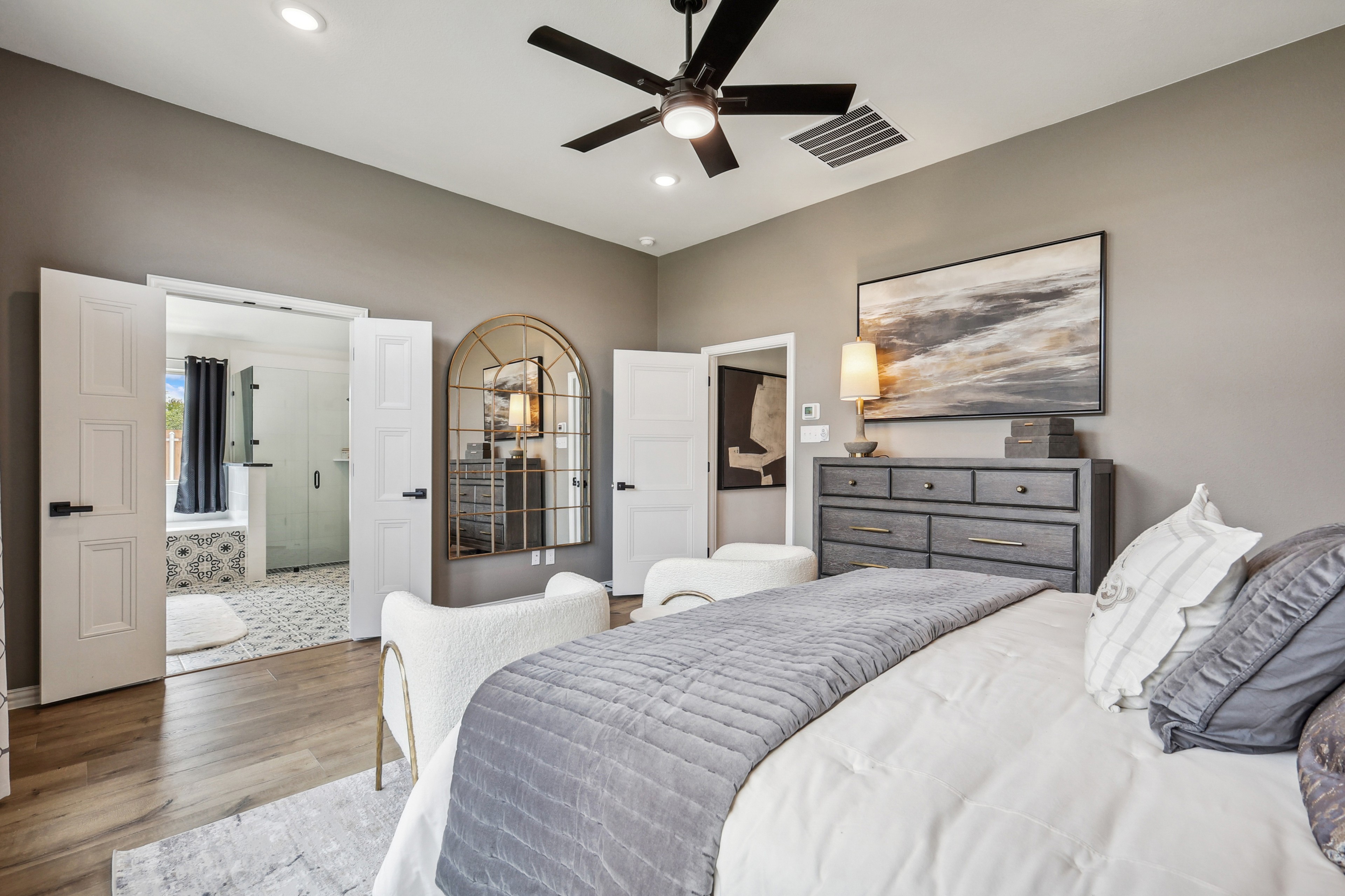 Luxurious bedroom with ensuite bath, large mirror, modern art, and wood floors in Churchill community.
