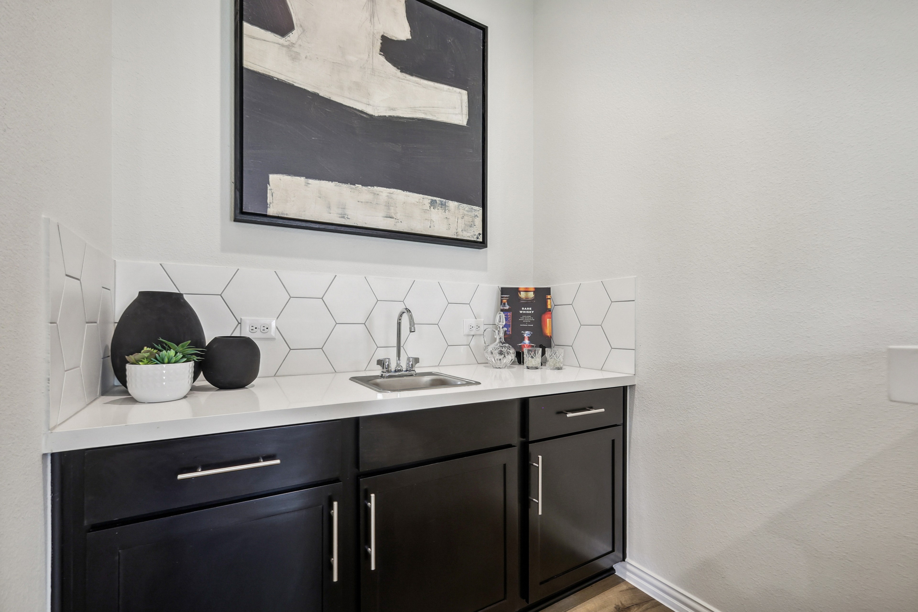 Small modern wet bar with hexagonal tile backsplash, sleek black cabinetry. Located in Churchill community.