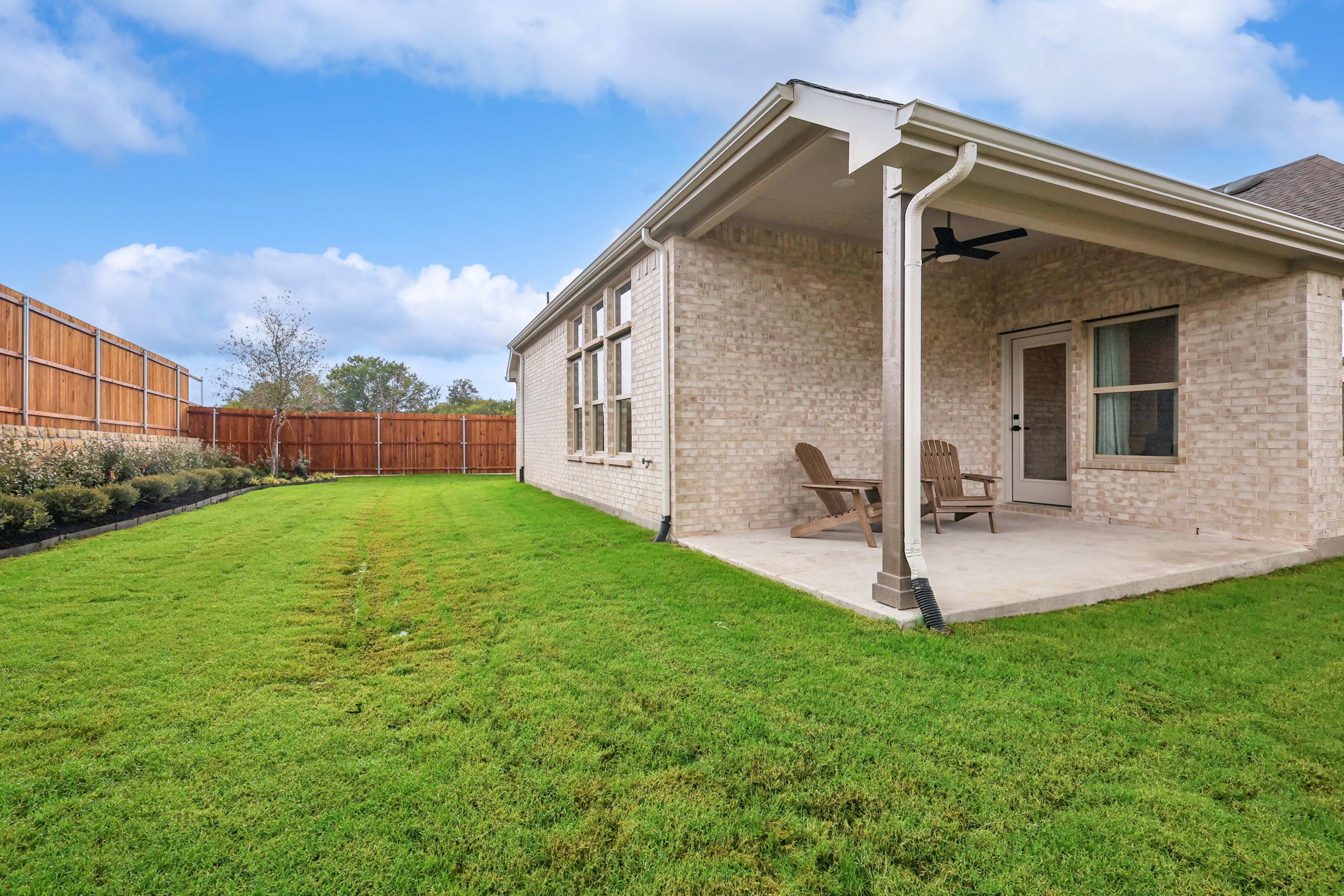 Spacious backyard with green lawn, covered patio, and brick facade in Churchill community. Modern fence and large windows.