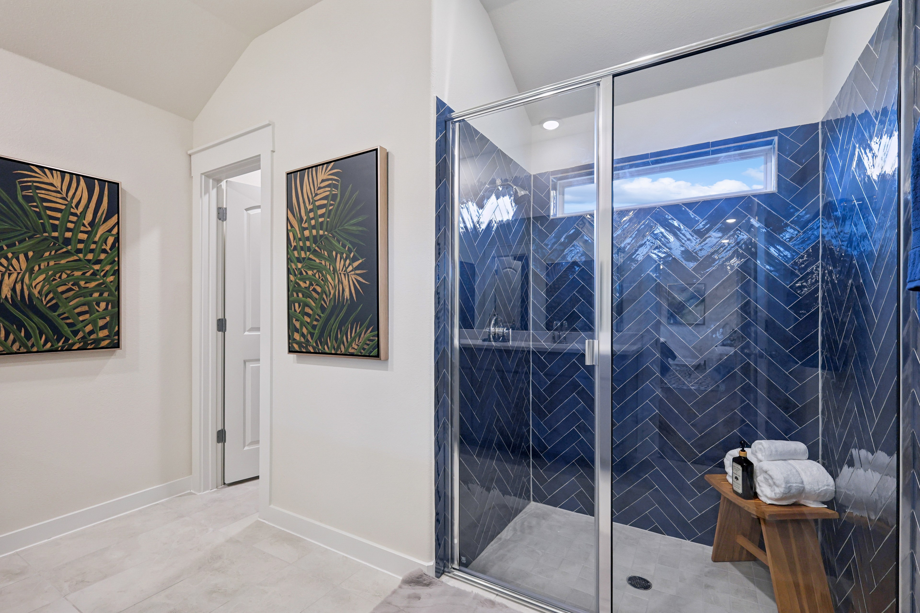 Modern bathroom with blue herringbone tiled shower, window, white door, and tropical wall art in Churchill community.