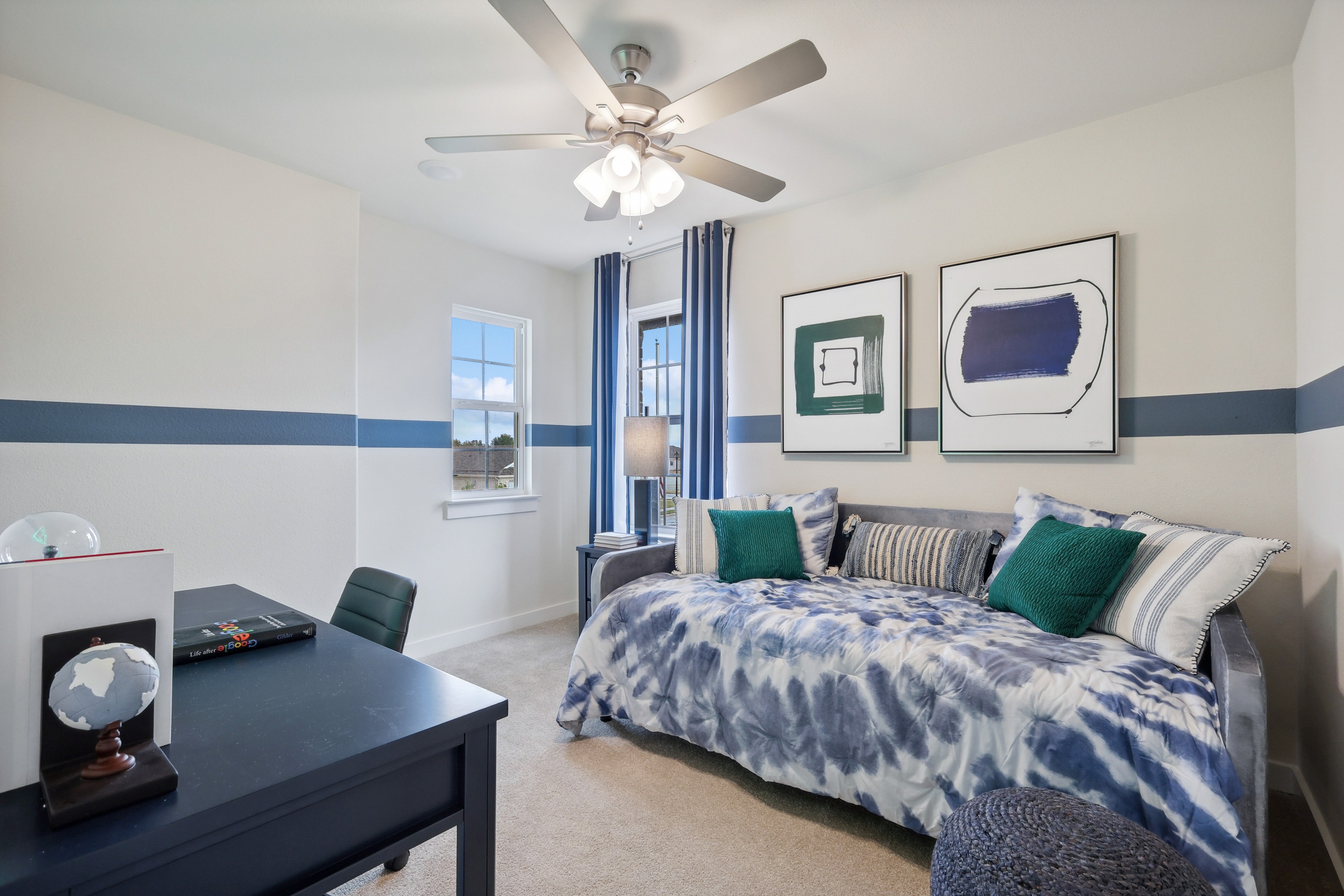 Modern room with blue-striped accents, bed, desk, art. Ceiling fan and window in Churchill community.
