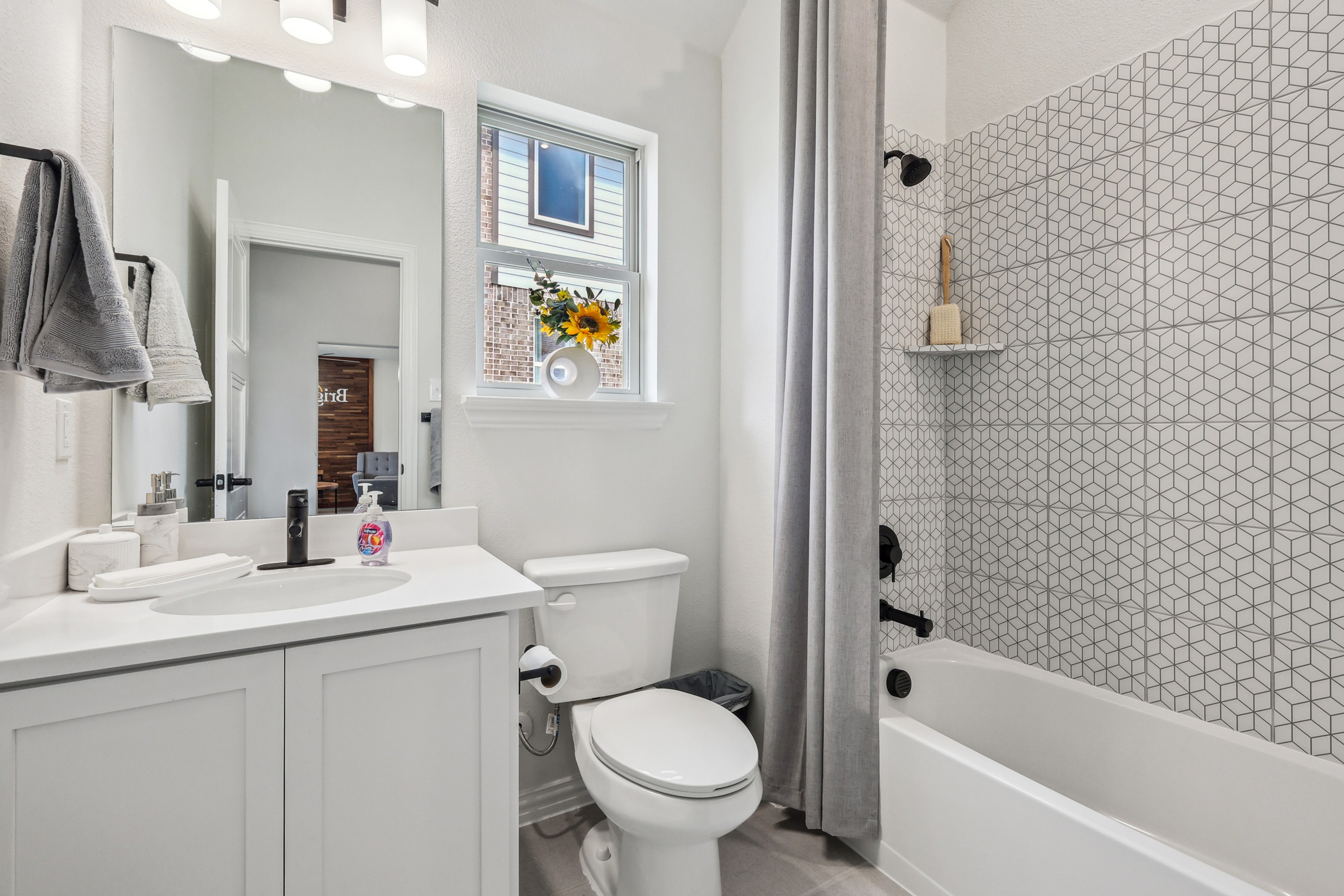 Modern bathroom with geometric tiles, gray curtains, and white fixtures in Churchill community. Bright, sleek design.