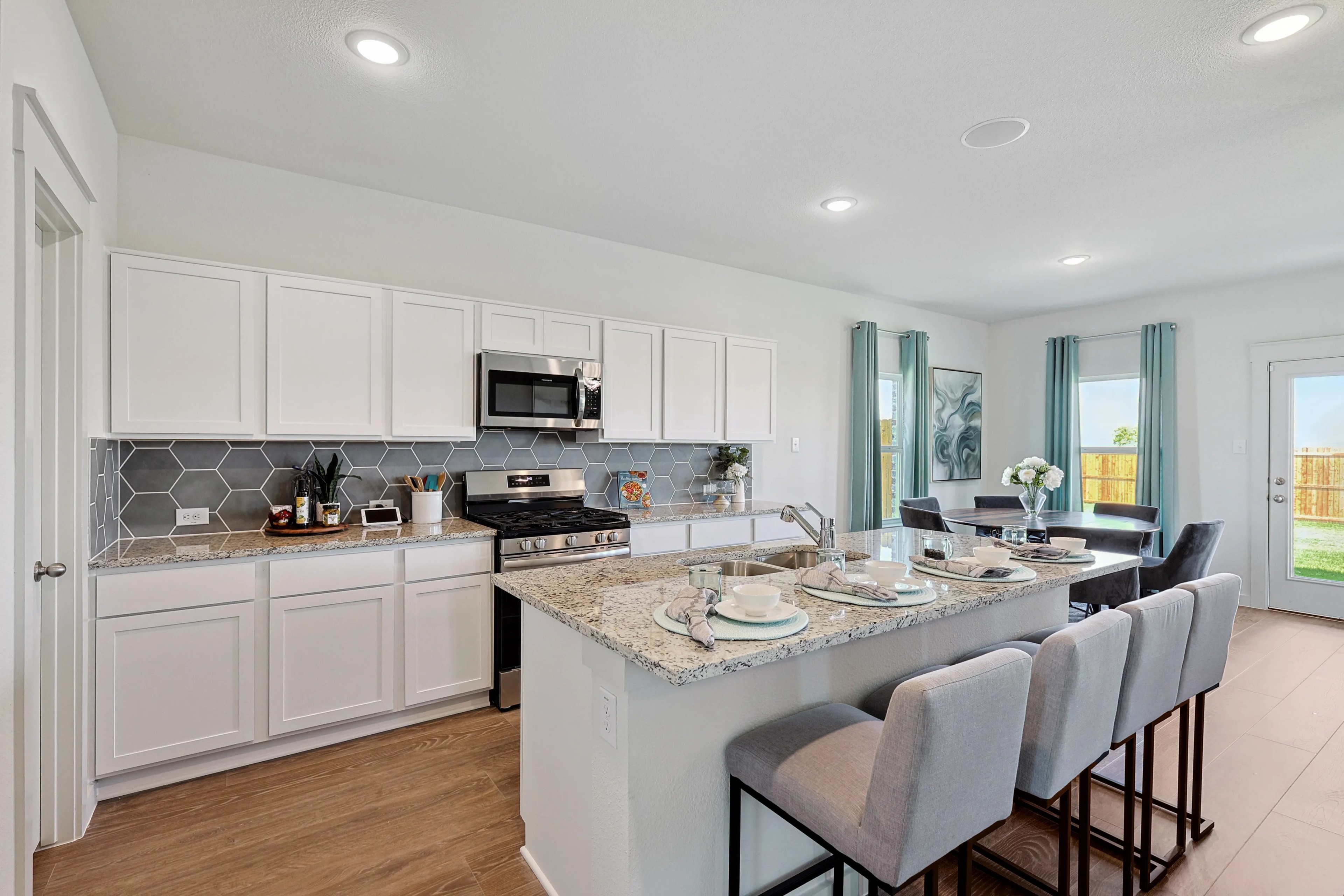 Modern kitchen in Patriot Estates with granite counters, hexagon tile backsplash, and open dining area.