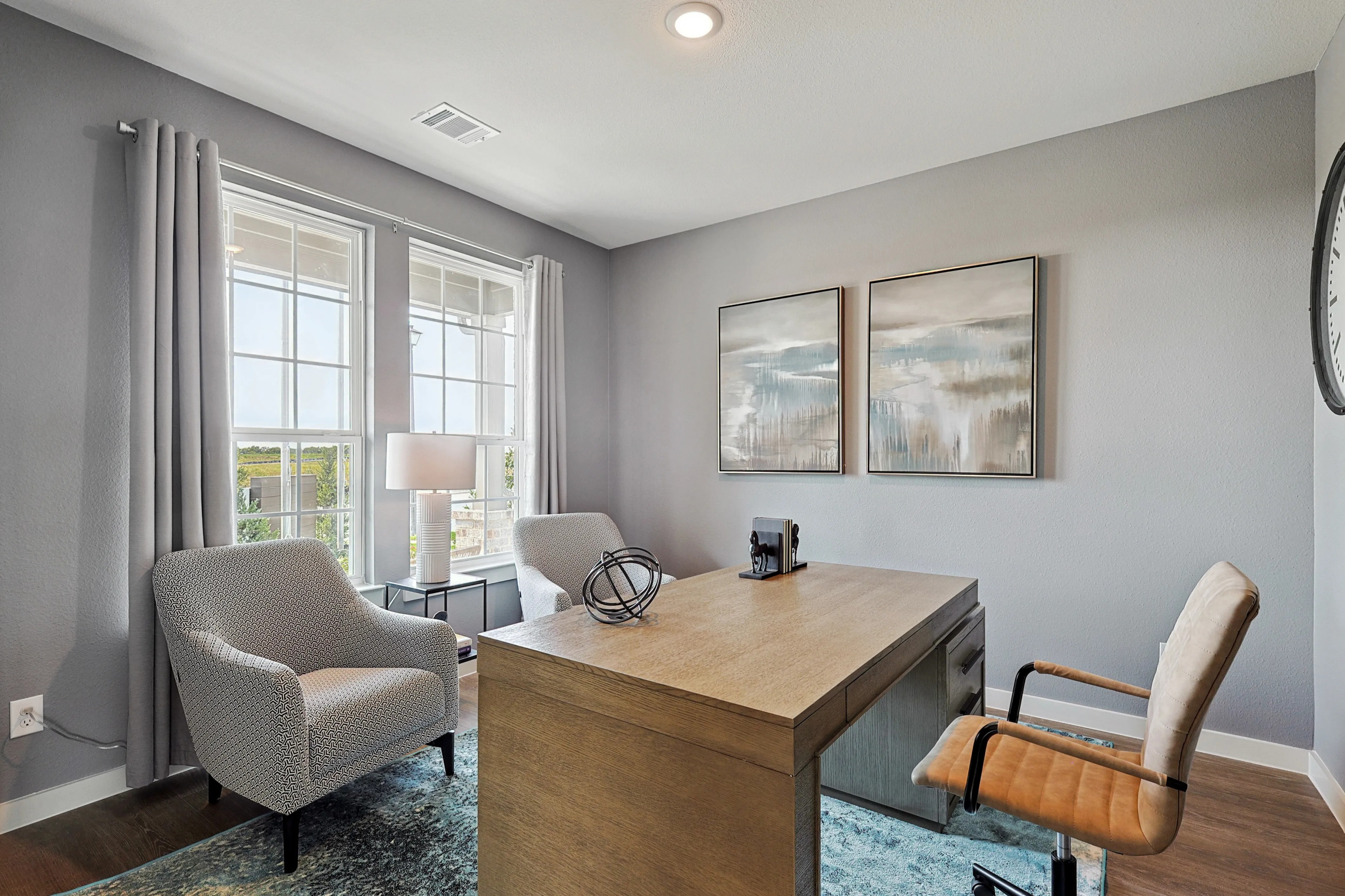 Modern home office with light gray walls, large windows, patterned chairs, and elegant artworks in Patriot Estates.