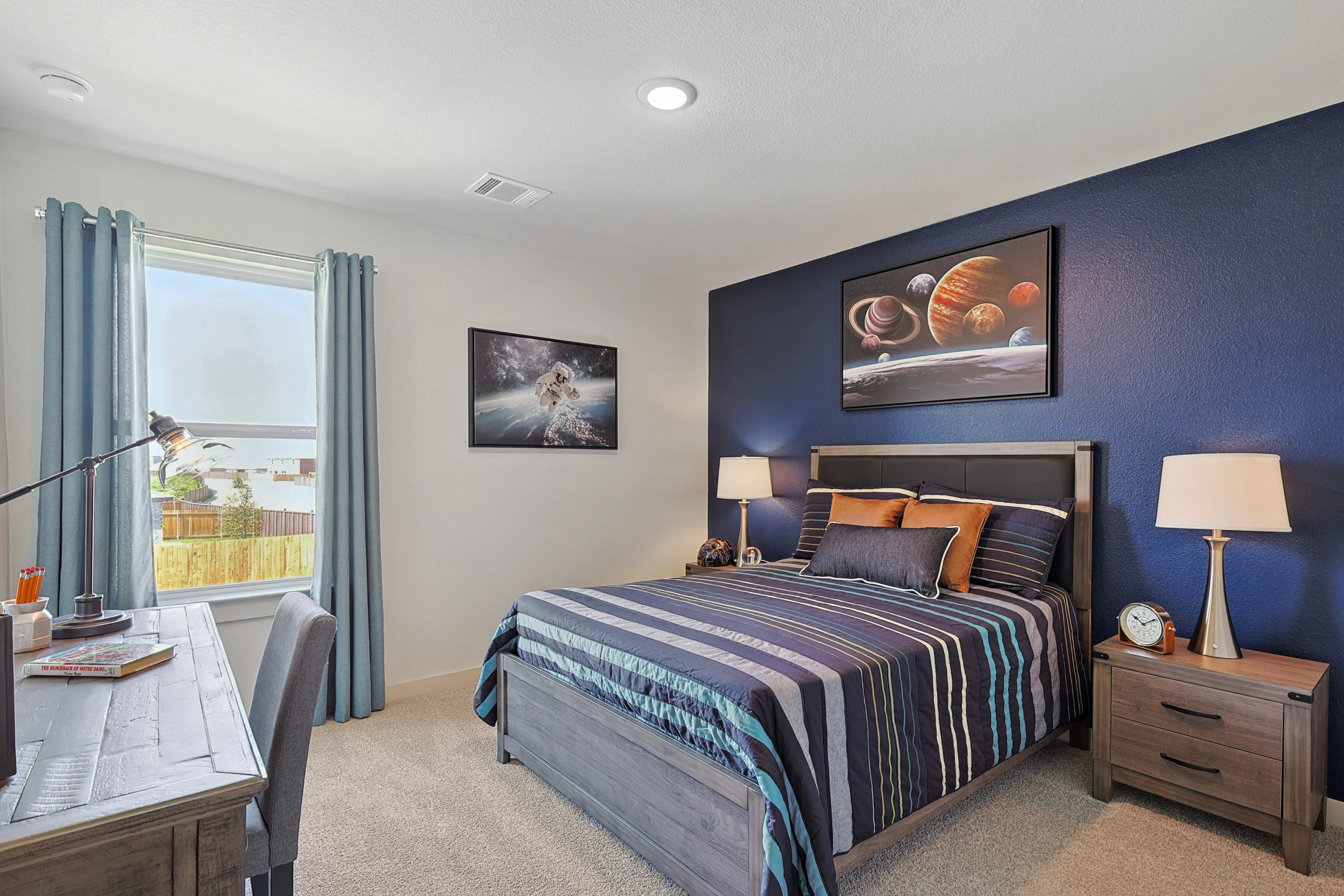 Modern bedroom with blue accent wall, space-themed decor, wood furniture in Patriot Estates.