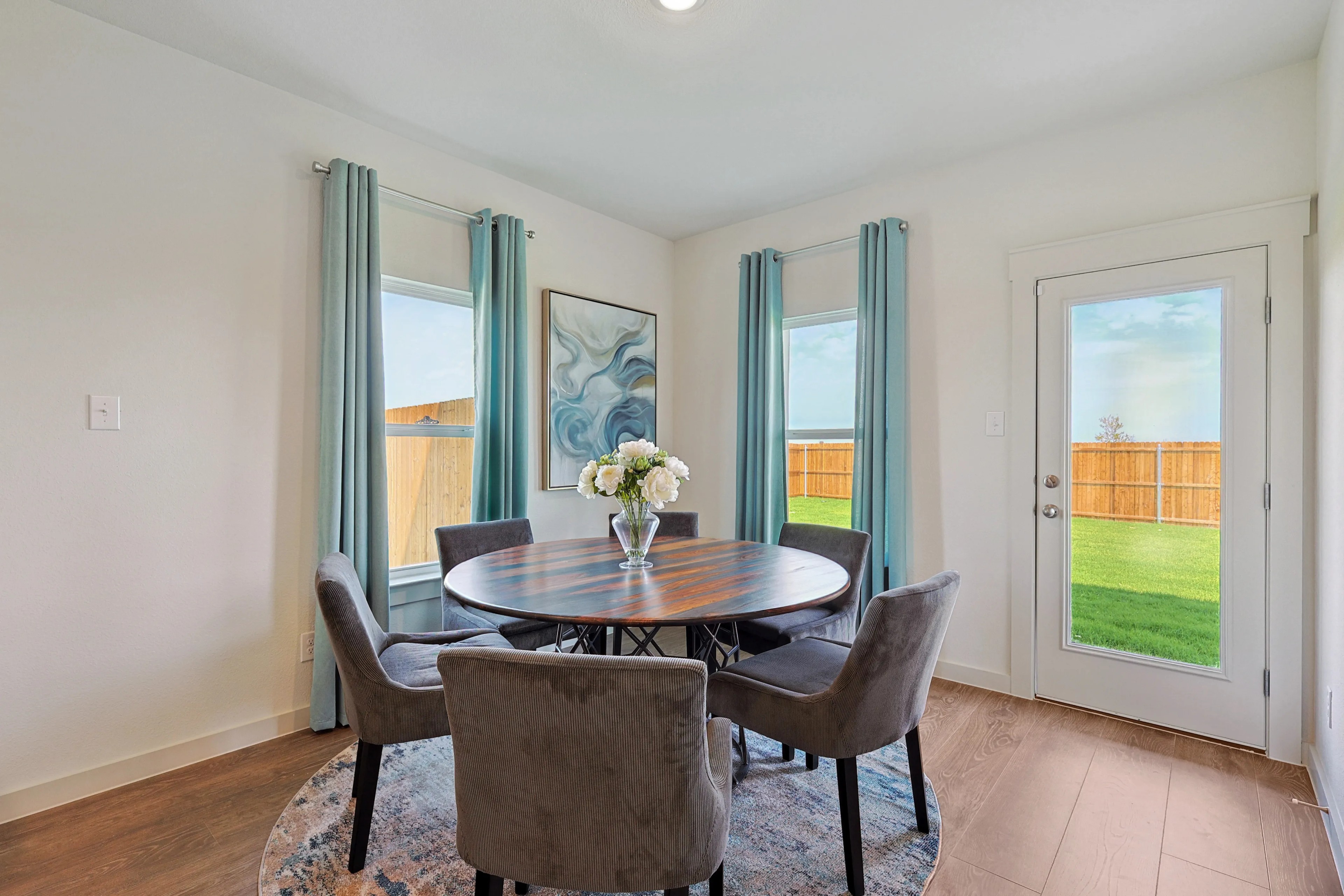 Elegant dining room with round wooden table, velvet chairs, large windows, artwork. Patriot Estates.