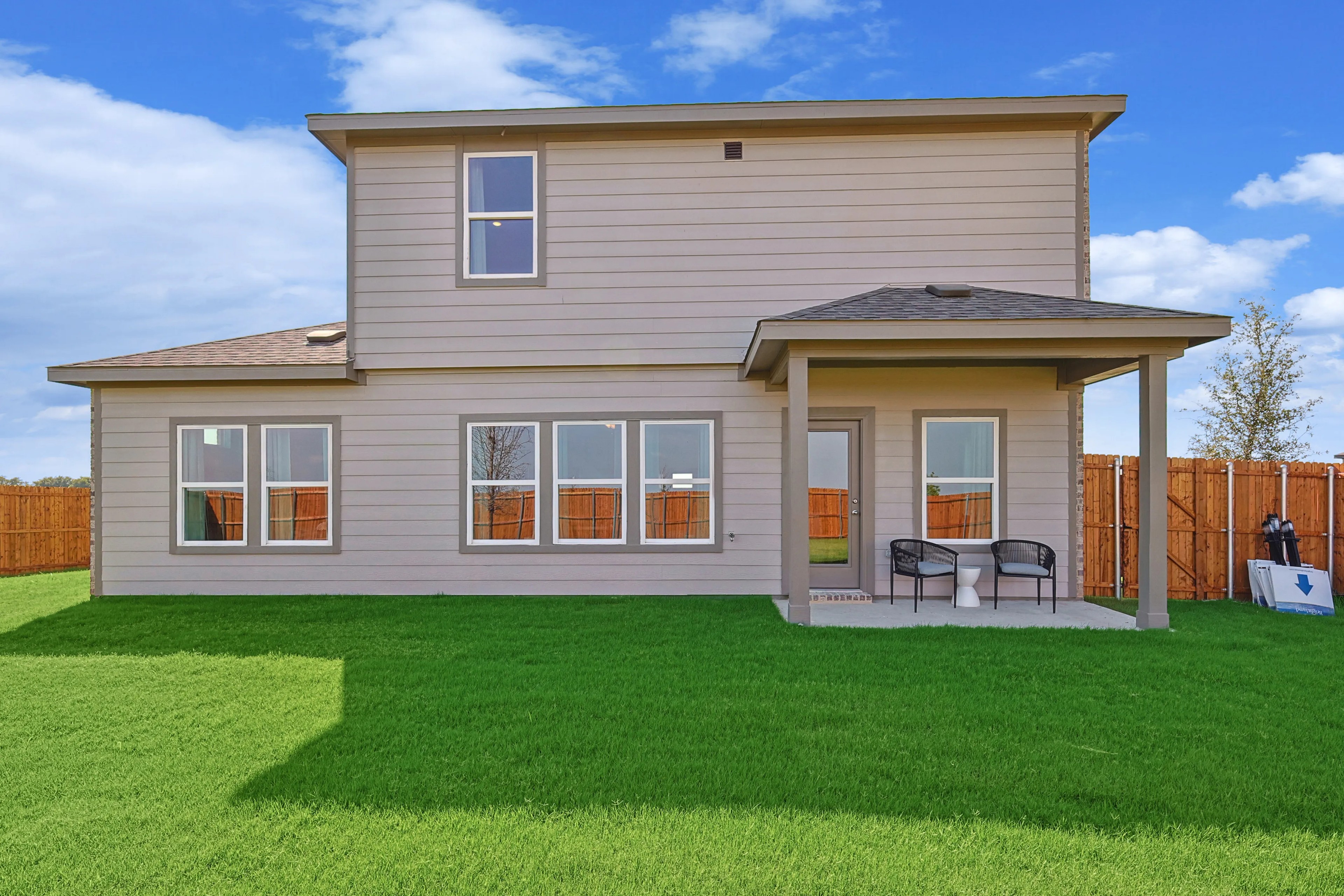 Modern two-story home with beige siding, large windows, and a small patio in Patriot Estates, Texas.