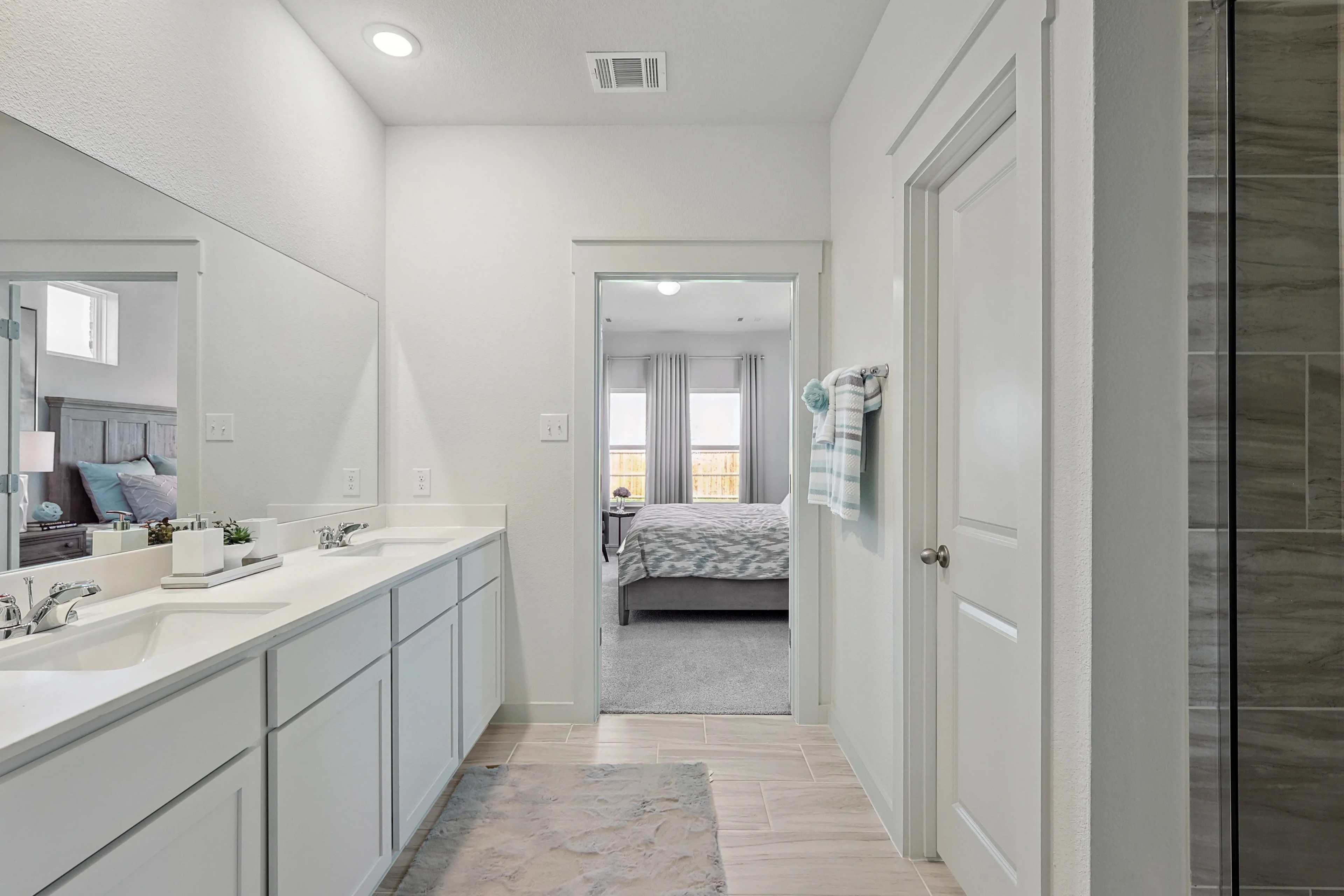 Spacious modern bathroom with double sinks, large mirror, neutral tones in Patriot Estates home visible through doorway.