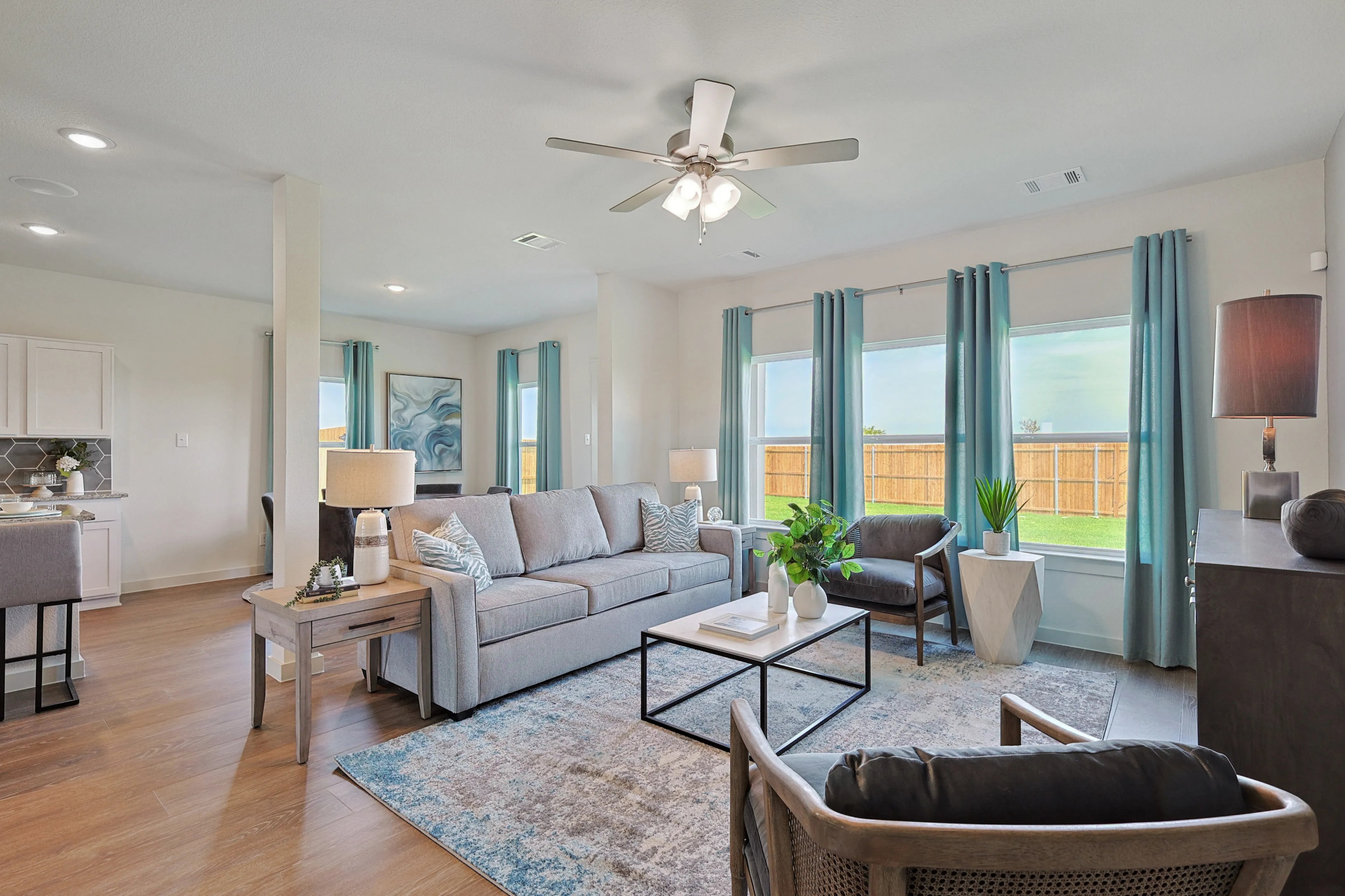 Modern living room with large windows, light wood flooring, cozy seating, Patriot Estates community.