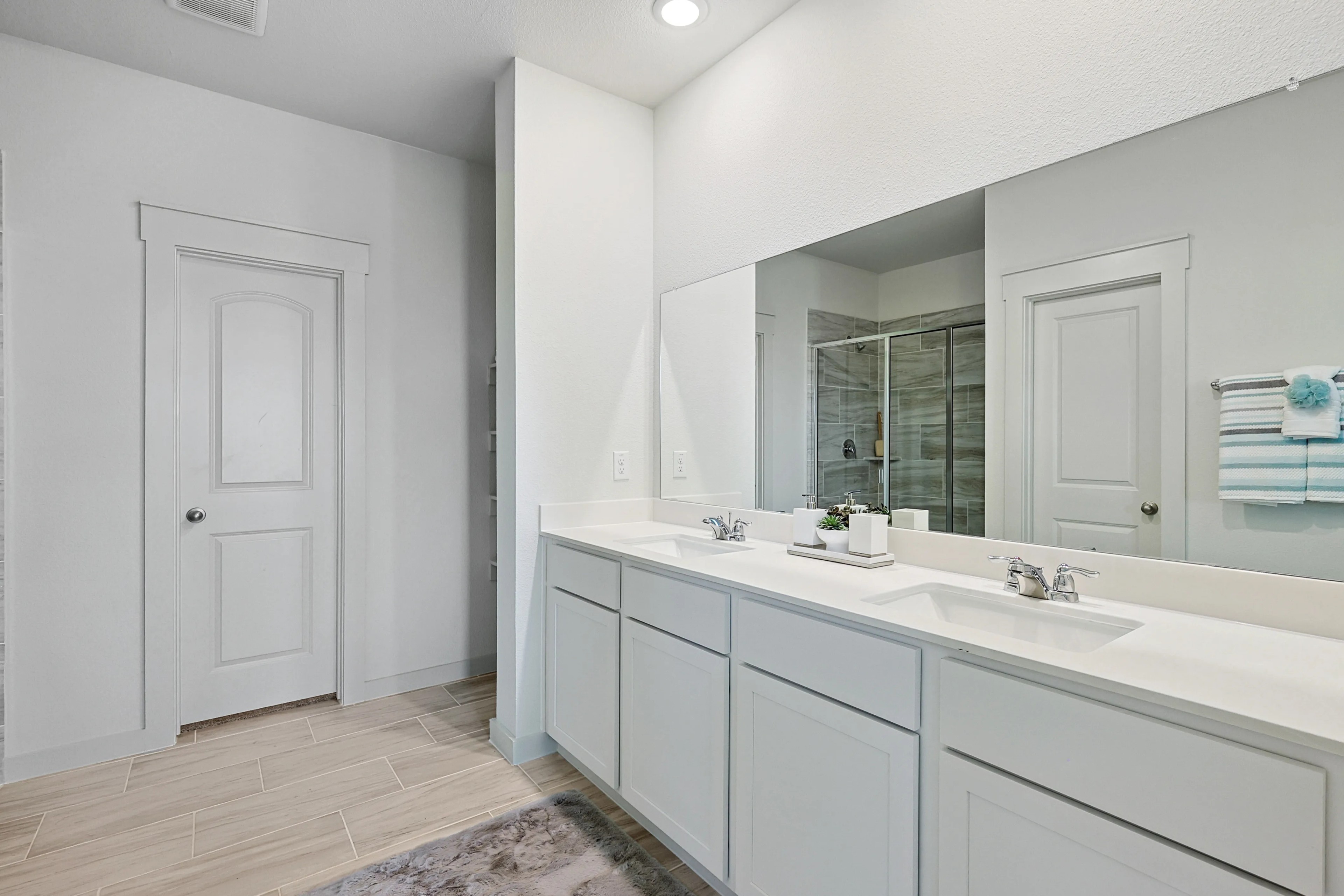 Modern bathroom in Patriot Estates with dual sink vanity, large mirror, glass shower, and wood tile flooring.