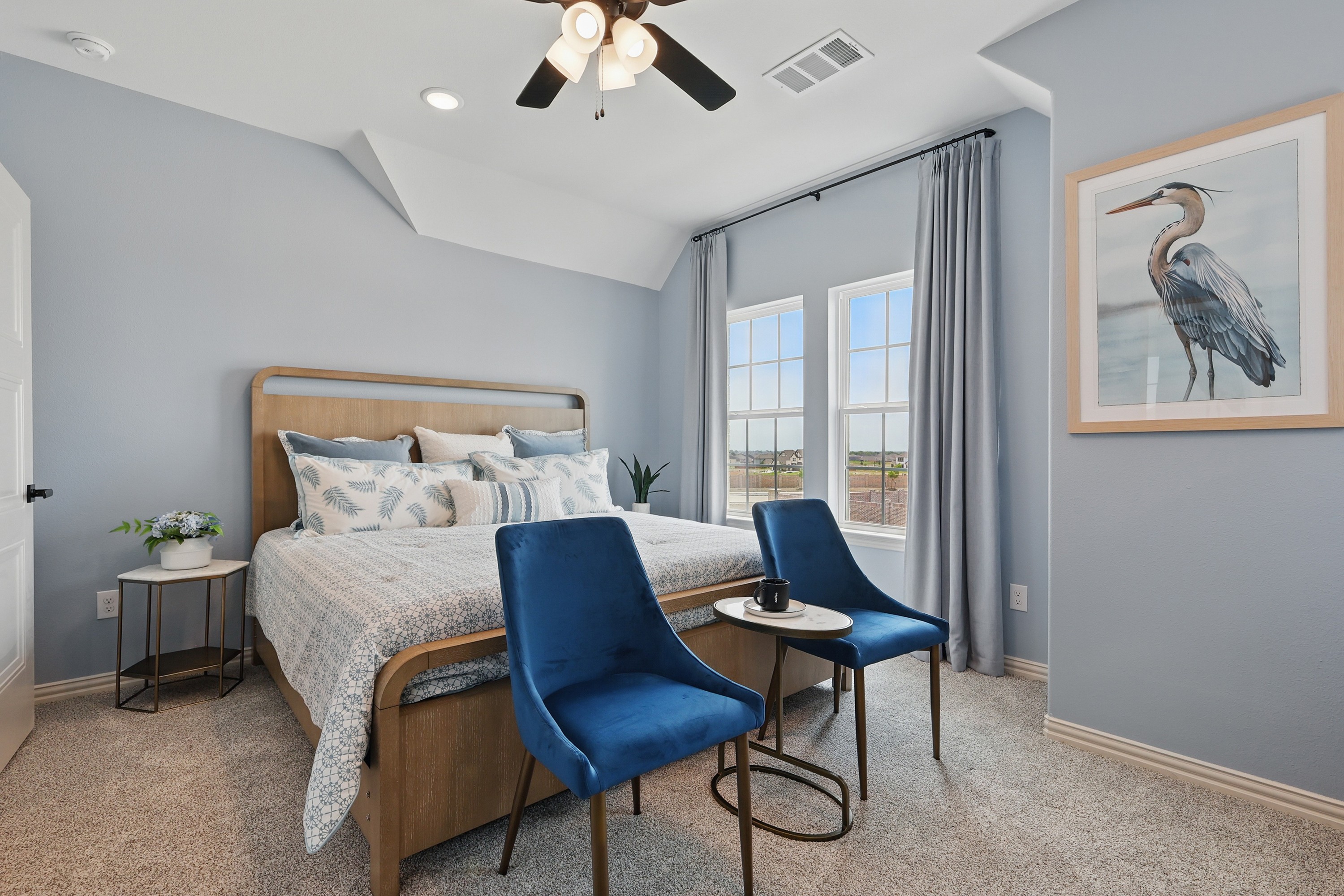 Elegant Westridge bedroom with blue velvet chairs, wooden bed, heron art, and large windows offering natural light.