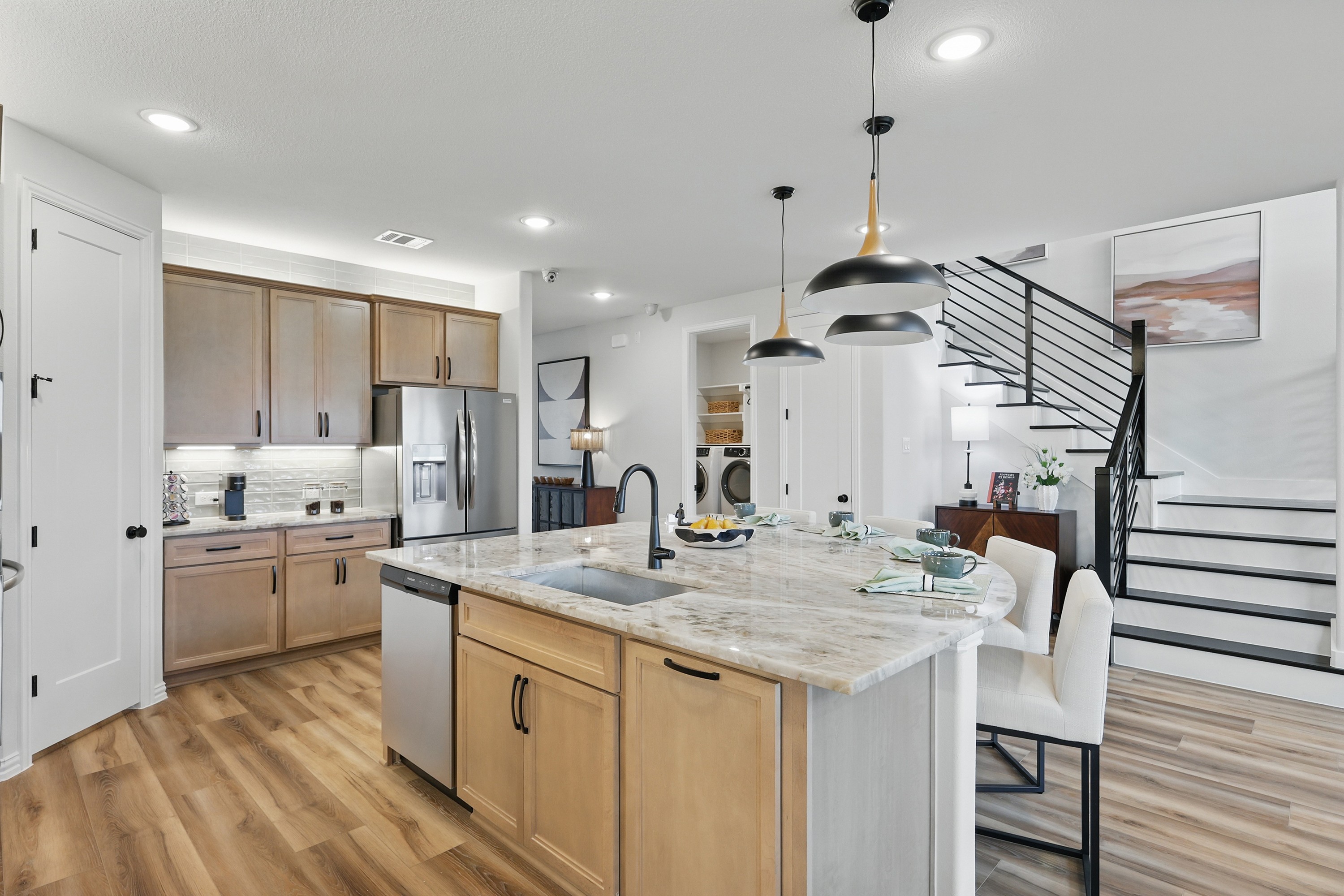 Modern kitchen in Westridge with marble island, pendant lights, and wood cabinets. Stylish staircase by dining area.