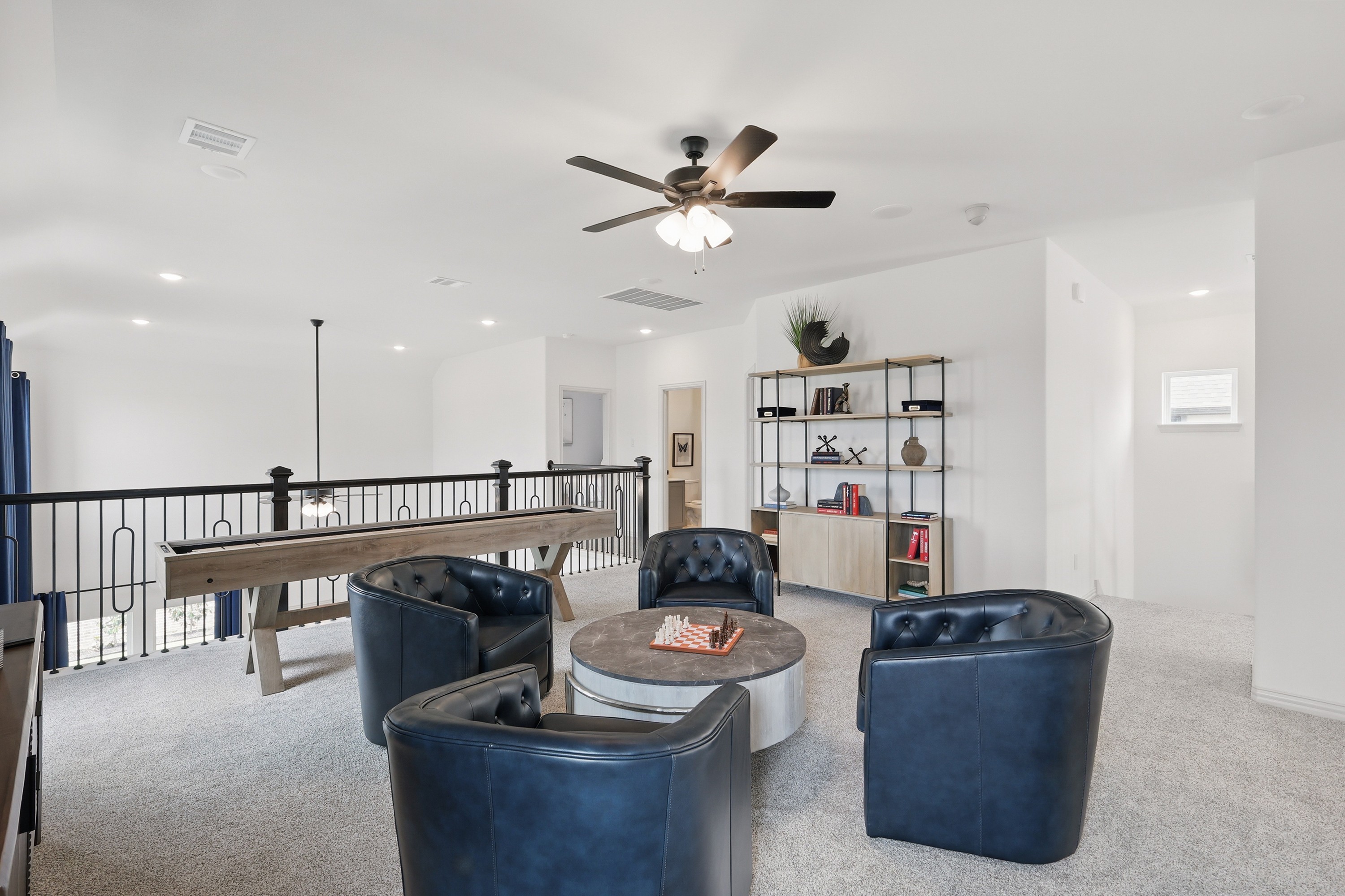Modern loft with plush blue chairs, sleek black railing, ceiling fan, bookshelf, Westridge, Texas.