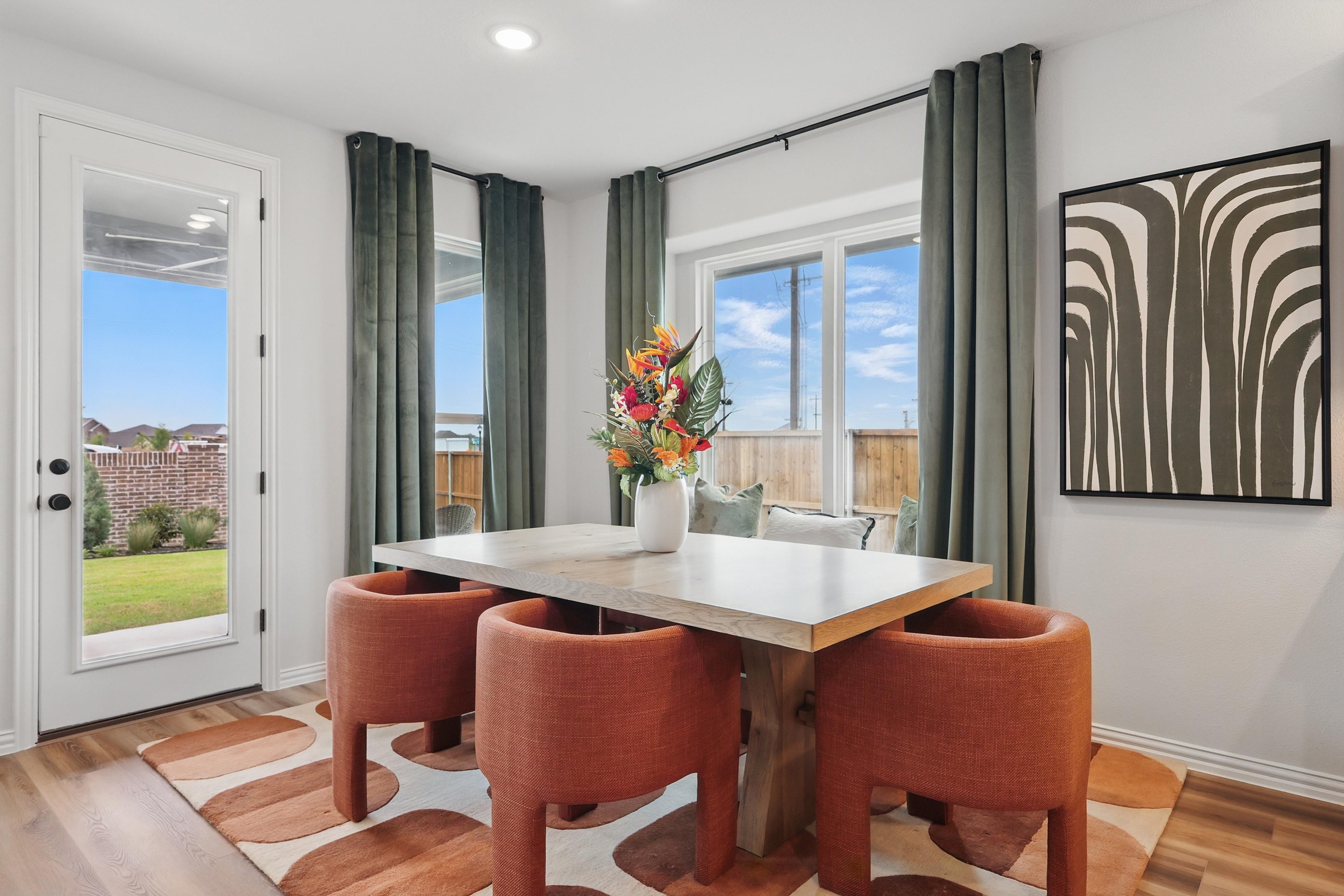 Dining nook with modern table, orange chairs, art piece, and garden patio view in Westridge community.