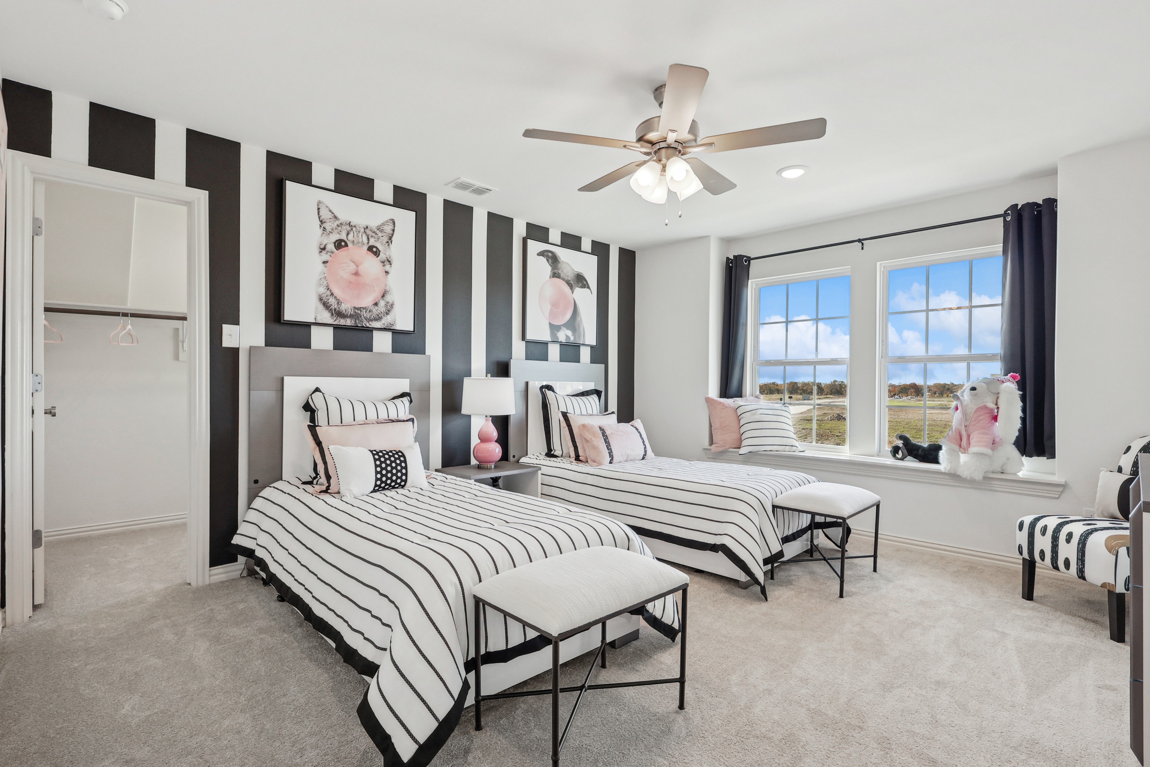Stylish twin bedroom with striped decor, playful artwork, and expansive windows in Bel Air Village community.
