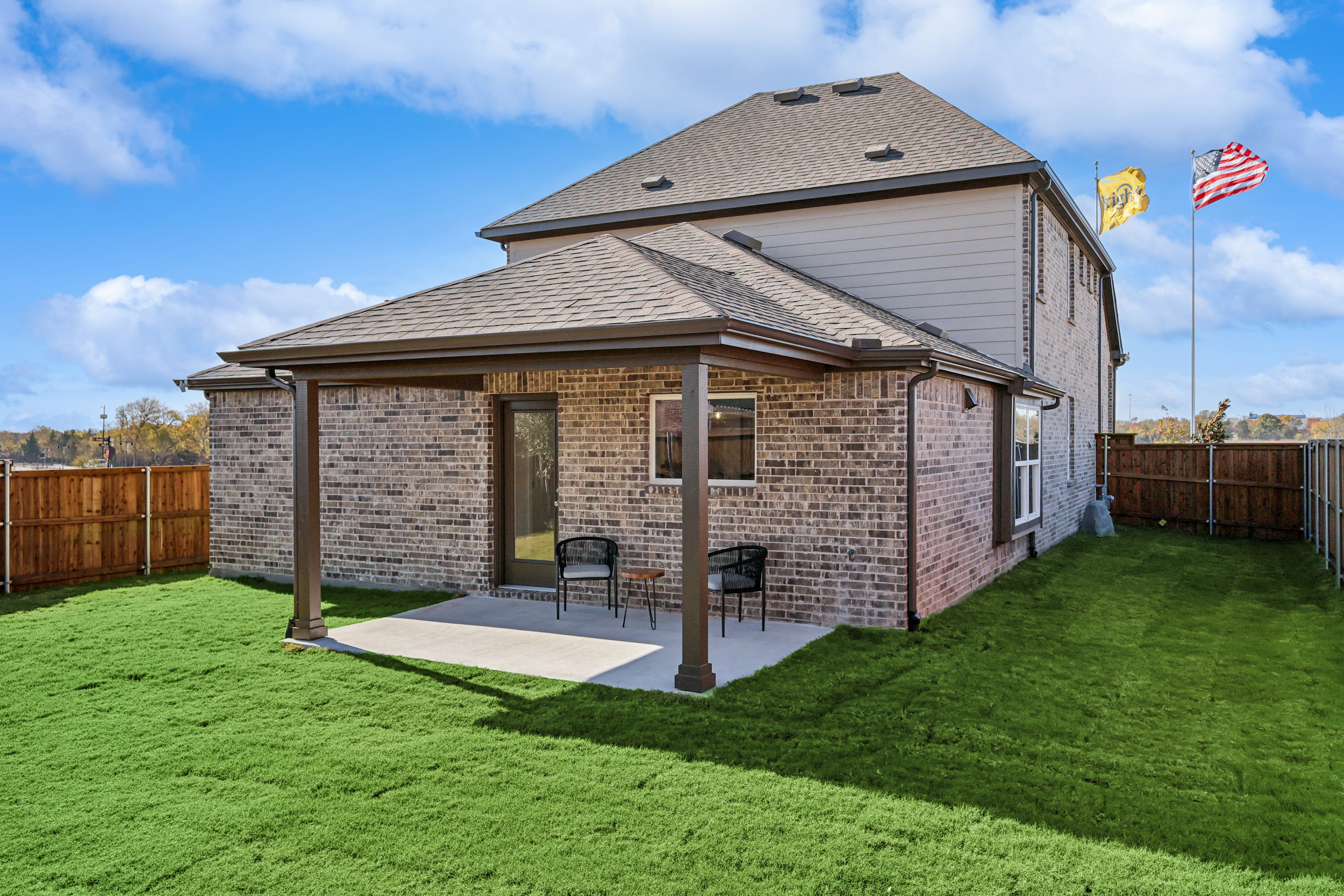 Modern brick house with covered patio, lush lawn, and fenced yard in Bel Air Village community.