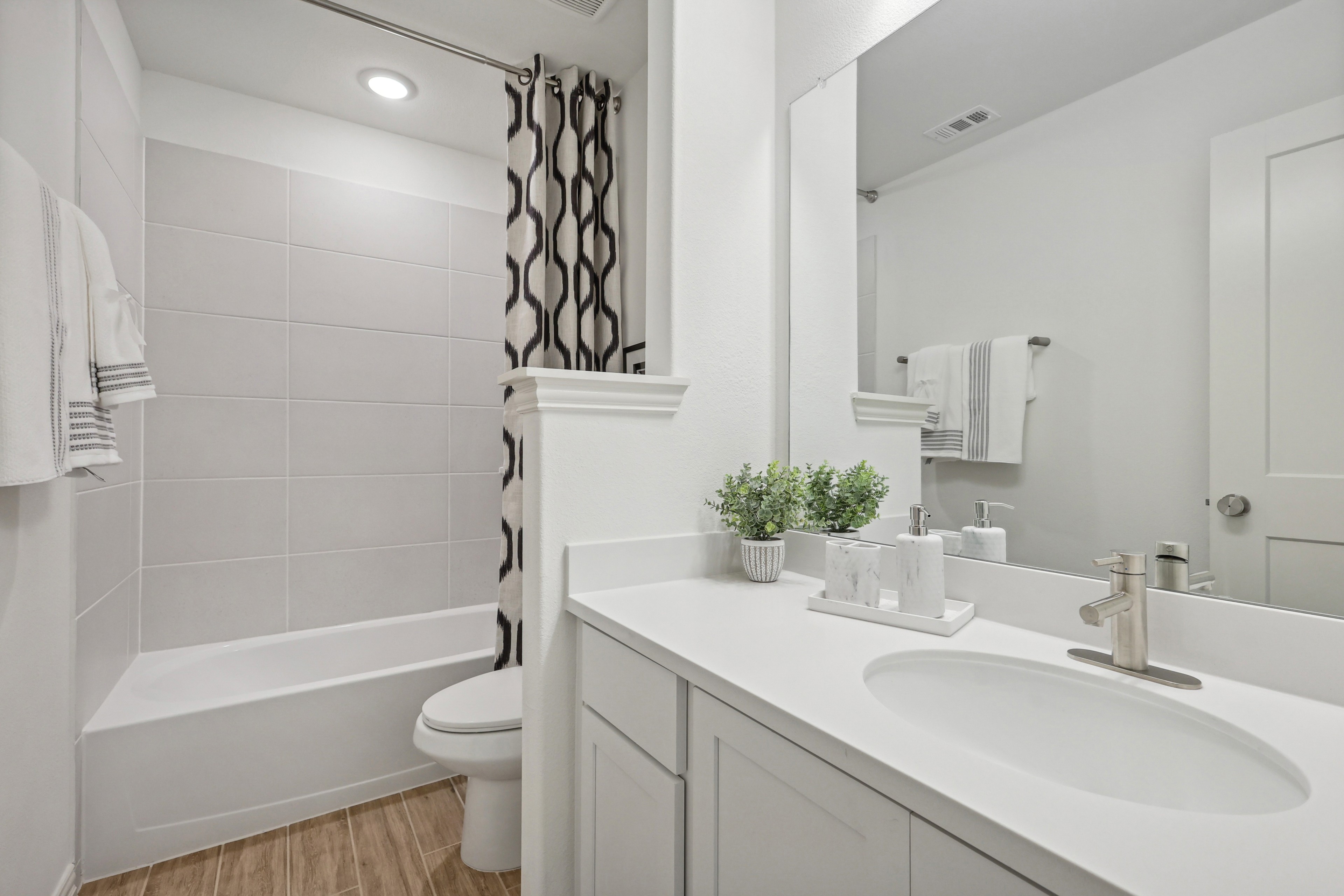 Modern bathroom with white vanity, oval sink, chrome faucet, large mirror, and stone-inspired tile in Bel Air Village.